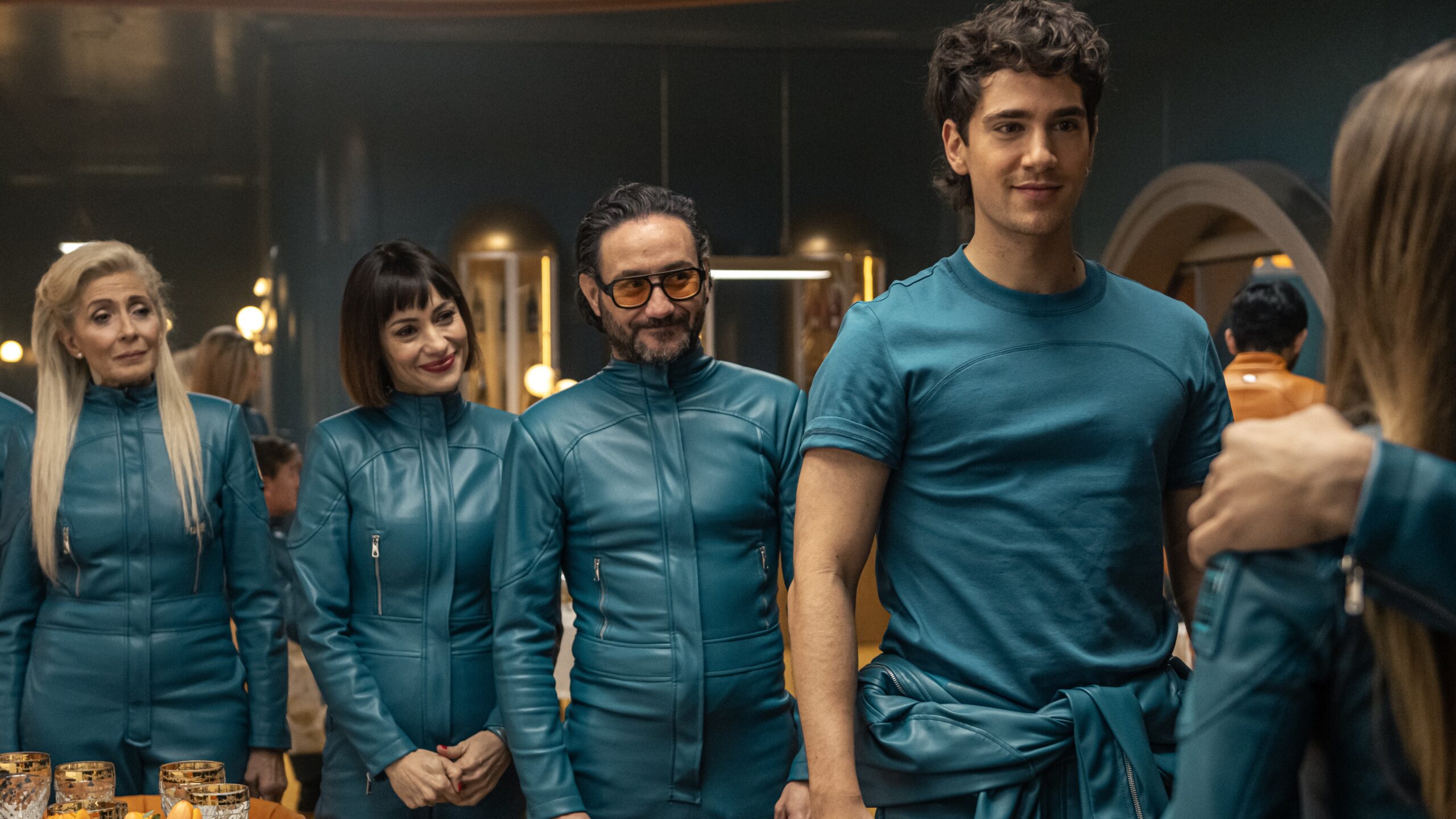 The cast of "Billionaires Bunker" cast in their blue jumpsuits in a scene from the Netflix show