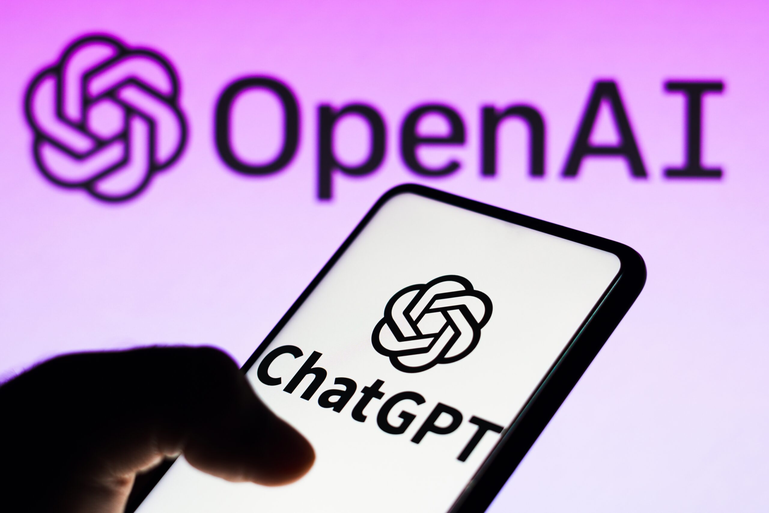 ChatGPT logo on a smartphone with the OpenAI sign in the background
