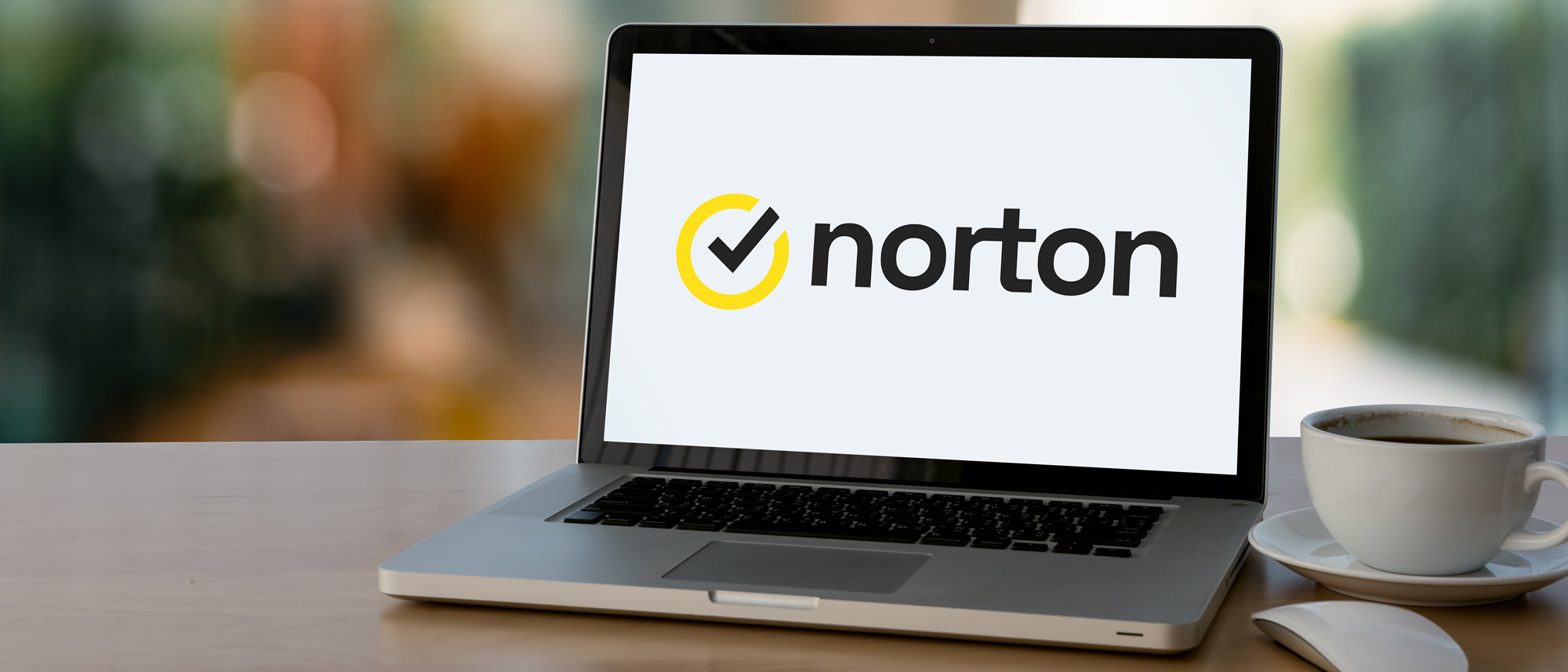 The Norton logo on a laptop next to a cup of coffee.