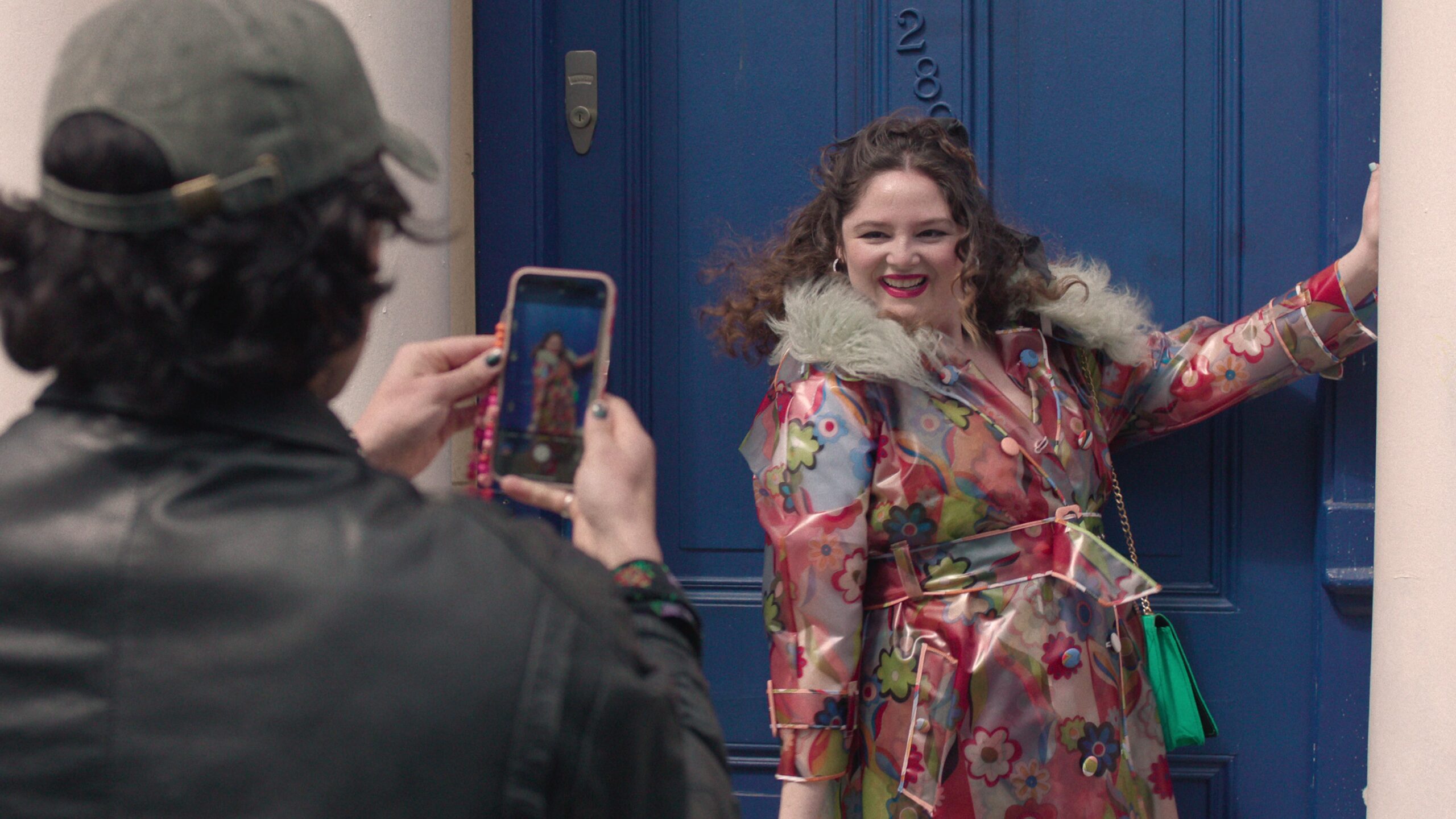 A man seen from behind takes a photo of Meg Stalter's character on his phone in a scene from Netflix's "Too Much"