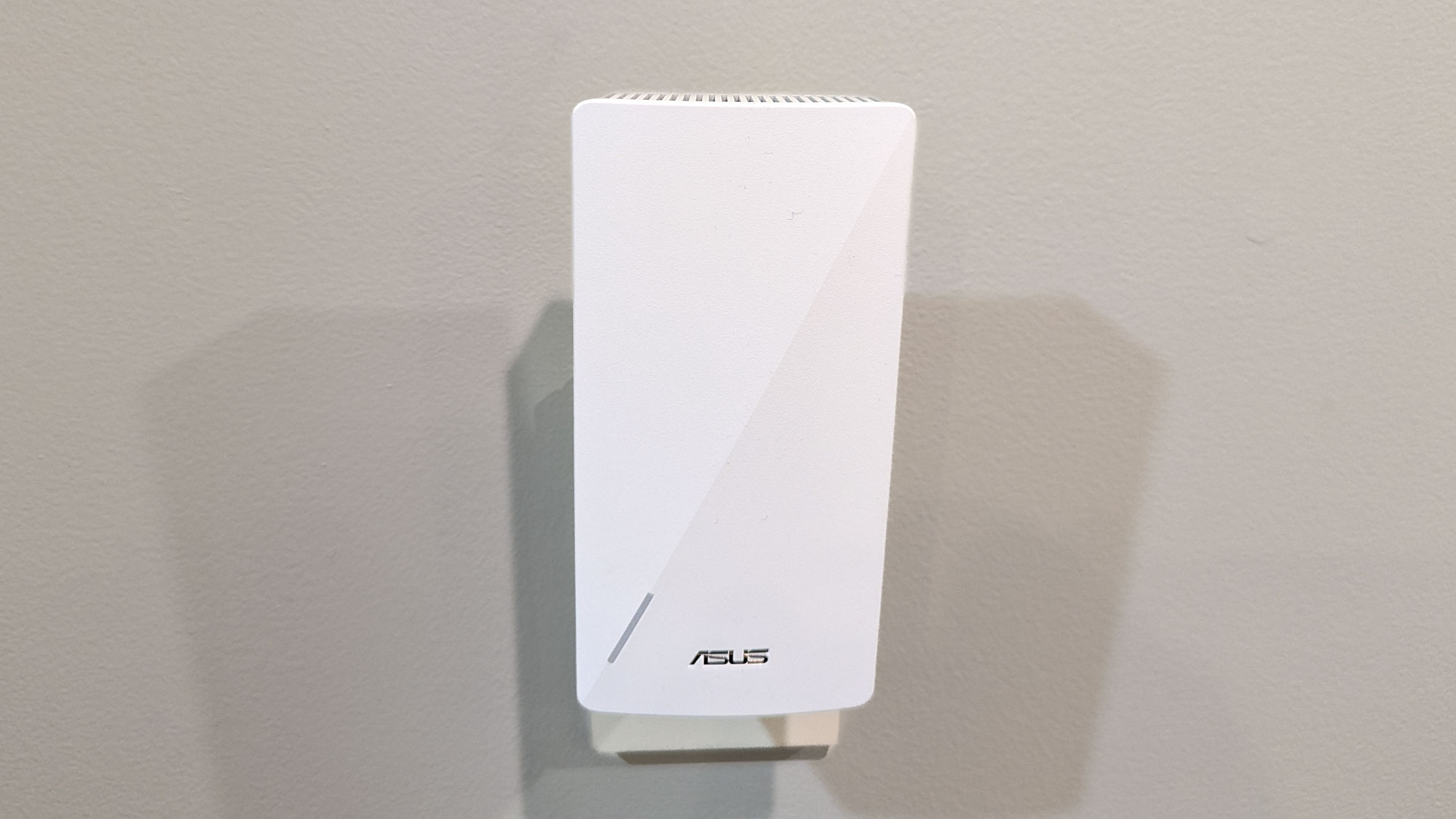 מקרוב מארח ASUS RP-AX58 Wi-Fi 6 מחובר לשקע קיר.