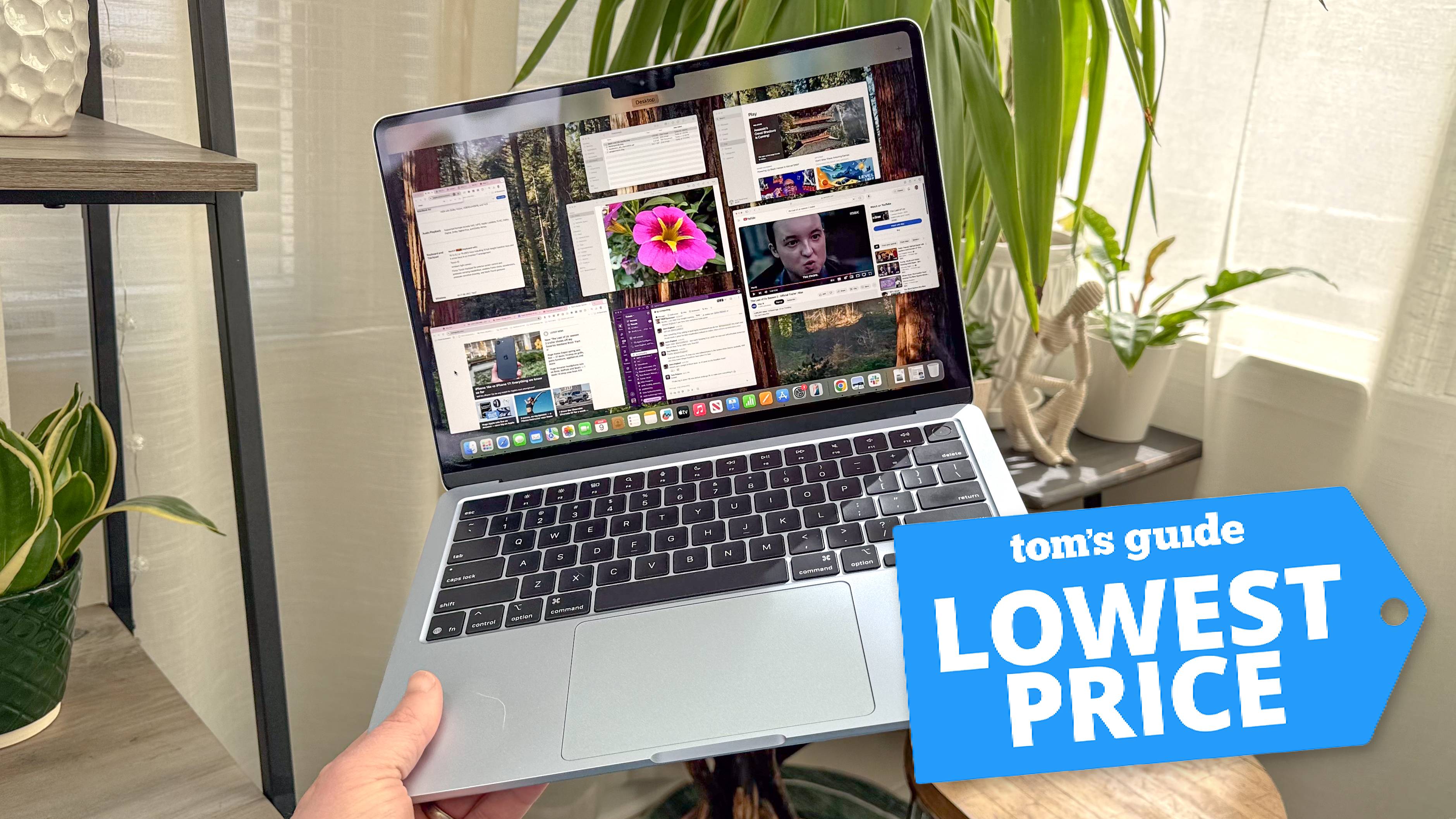 MacBook Air M4 ביד בחדר עם צמחים ברקע עם תג המחיר הנמוך ביותר של טום