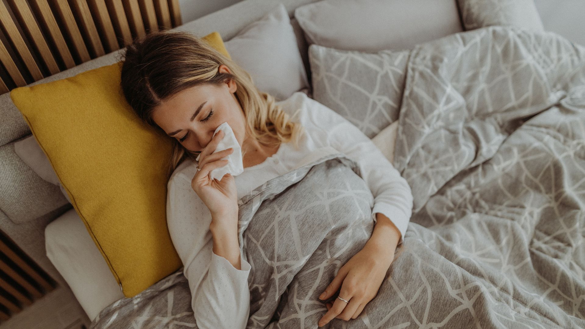 אישה עם קדחת השחת מנגבת אף סתום במיטה