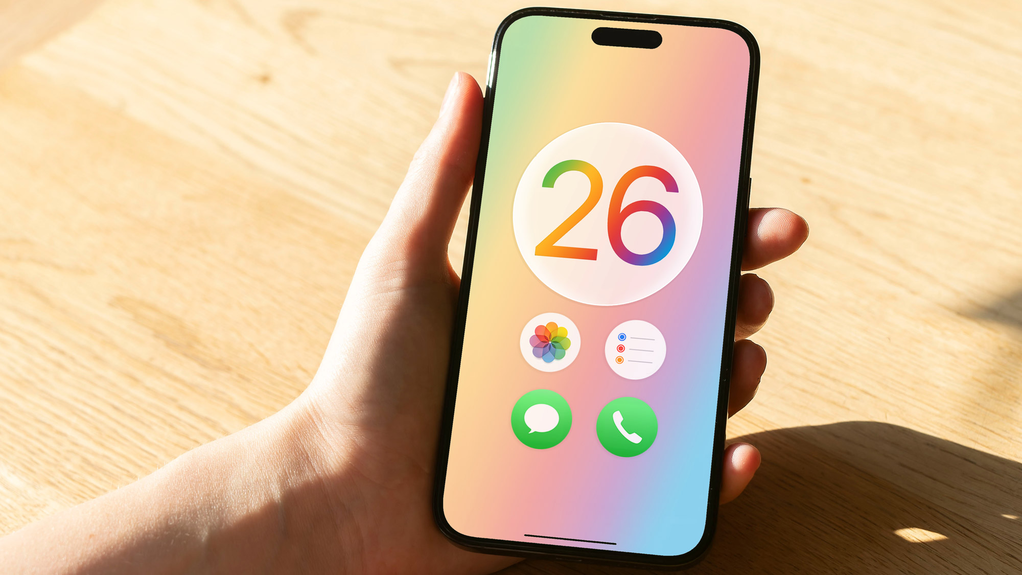 A render of the Apple iOS 26 logo with circular app icons on an iPhone held in a hand.