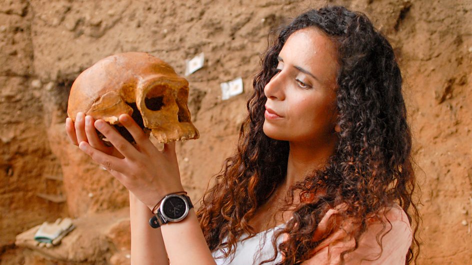 A promotional image for 'Human' showing paleoanthropologist Ella Al-Shamahi holding Irhoud 1 skull cast in Morocco.
