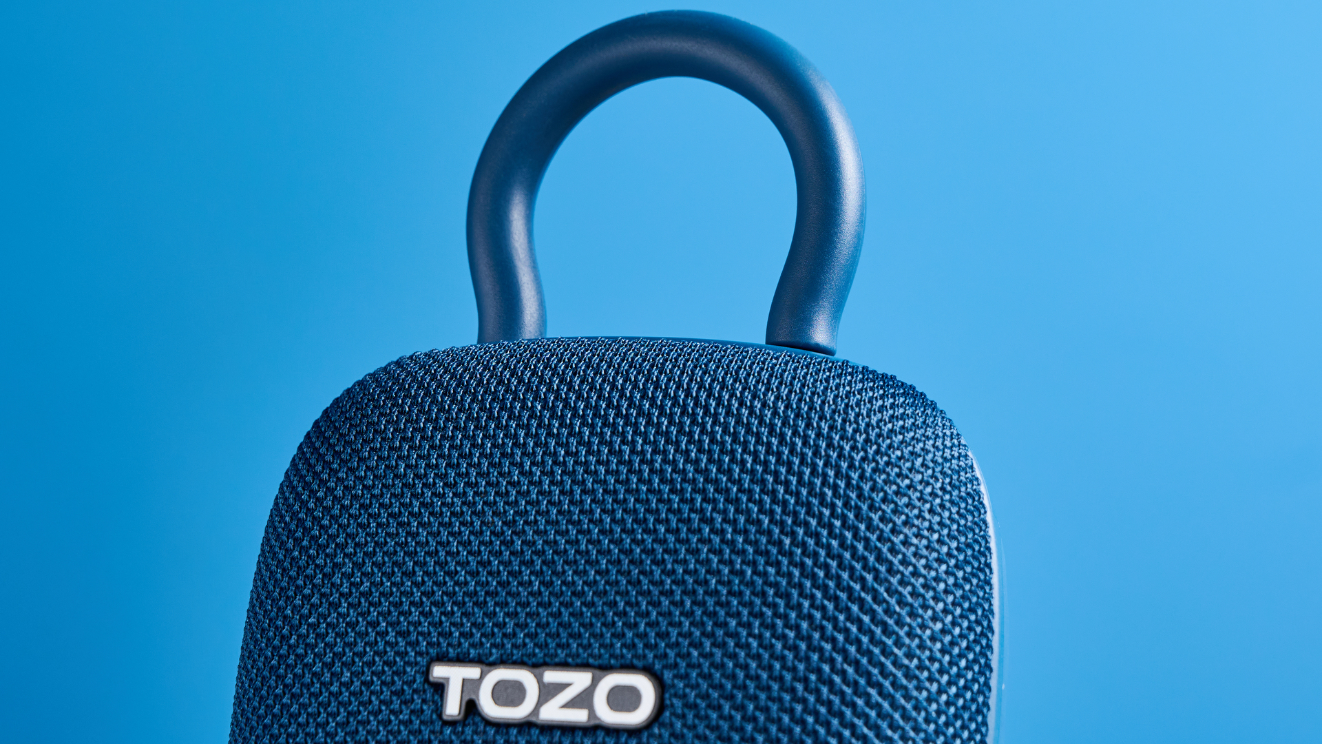 רמקול TOZO PE1 בכחול עם קליפ מובנה שצולם על רקע כחול.