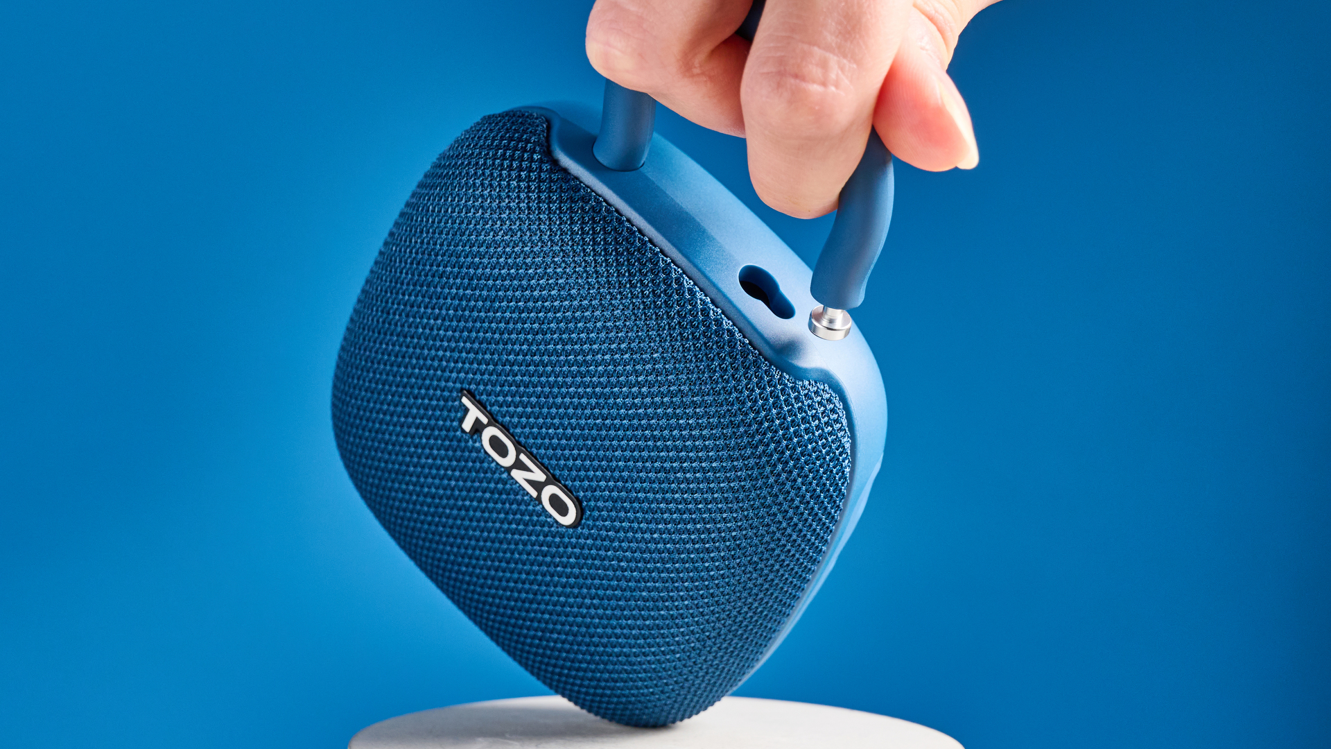 רמקול TOZO PE1 בכחול עם קליפ מובנה שצולם על רקע כחול.