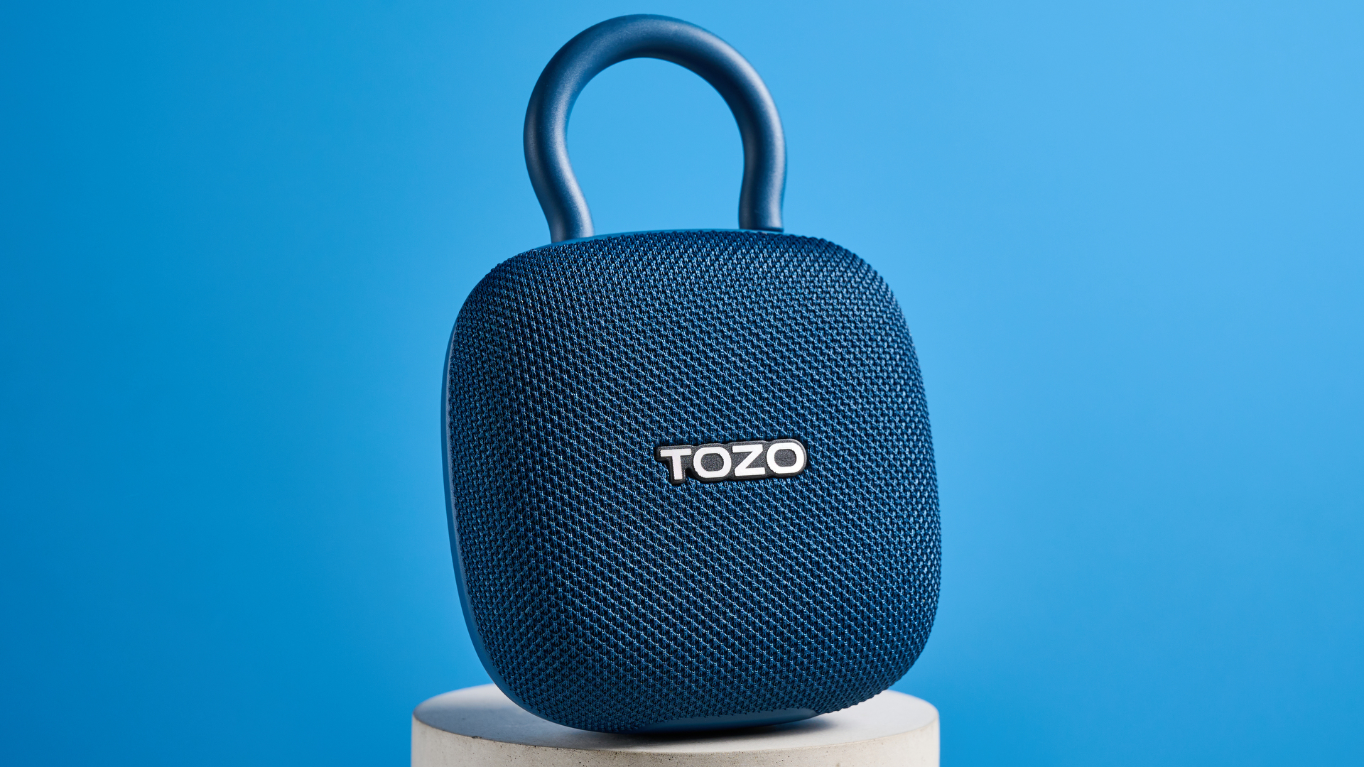 רמקול TOZO PE1 בכחול עם קליפ מובנה שצולם על רקע כחול.