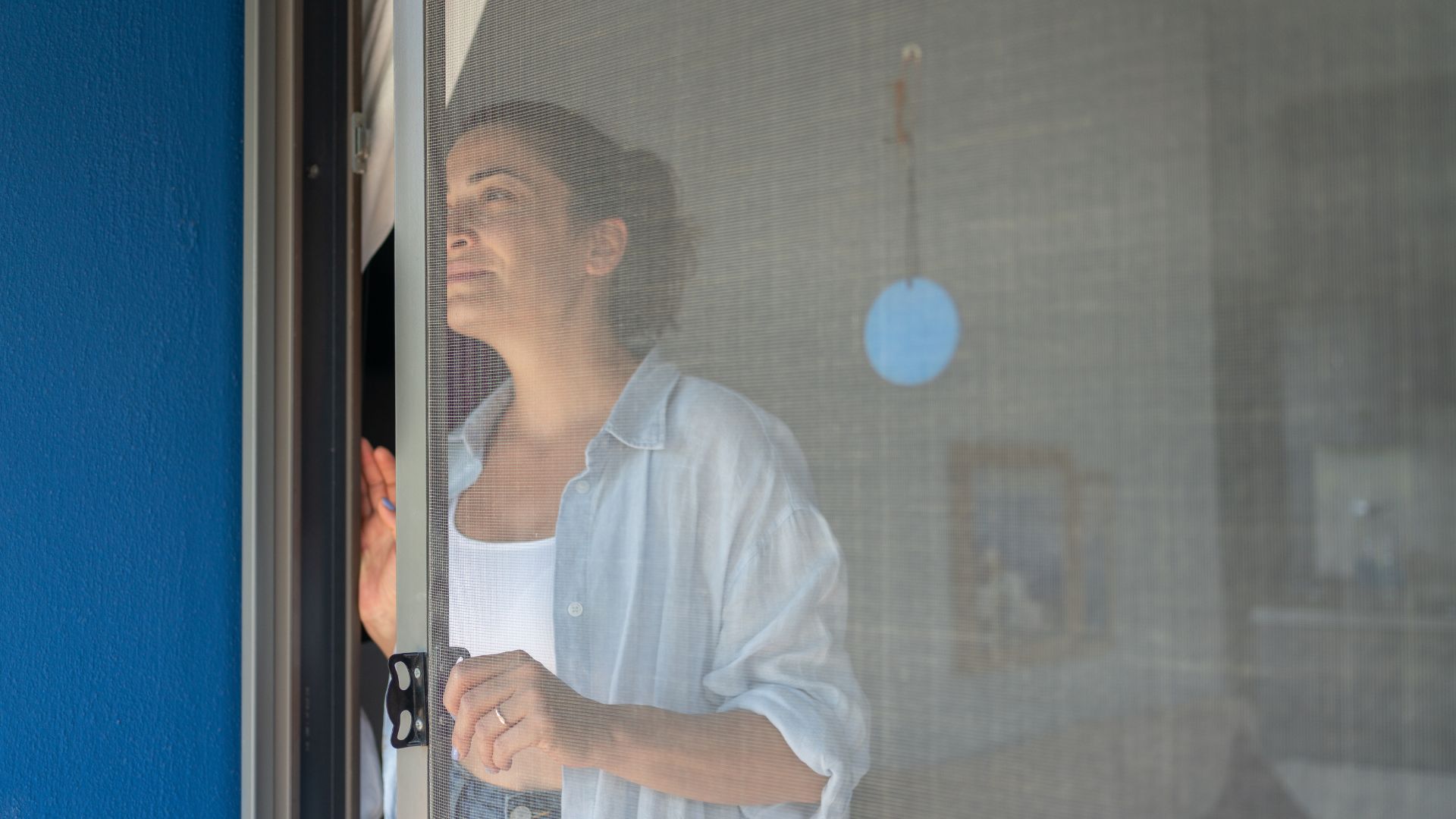 אישה ברונטית פותחת חלון עם מסך יתוש. 