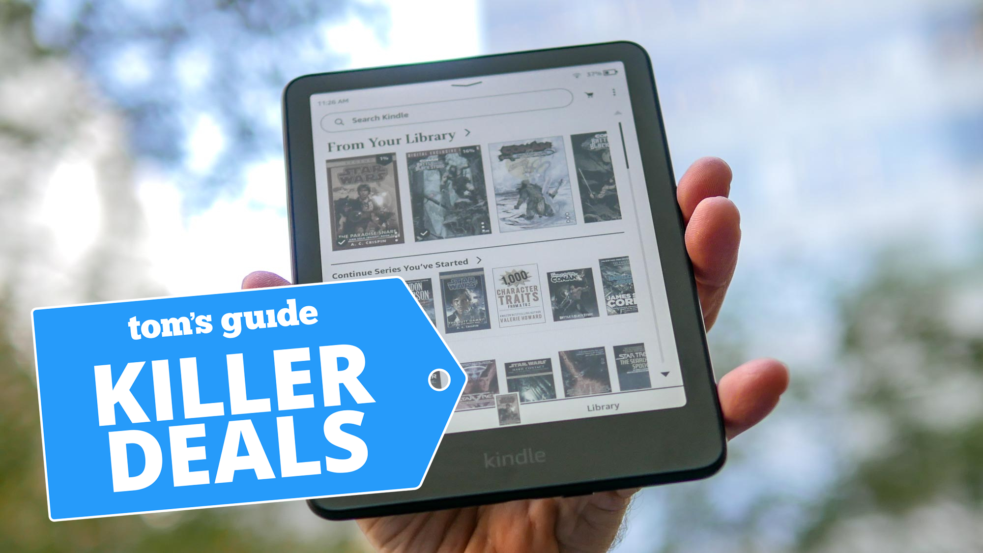 Kindle Colorsoft מוחזק ביד עם עצים ברקע