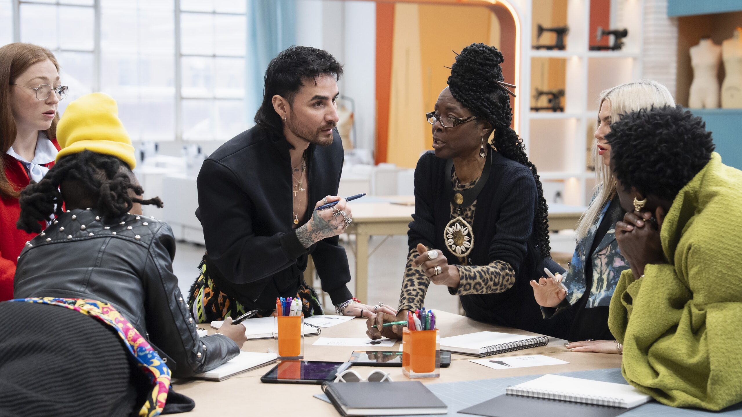 A stylishly attired group of new contestants lean in as they discuss their fashion-forward designs for a "Project Runway" challenge in "Project Runway" season 21.