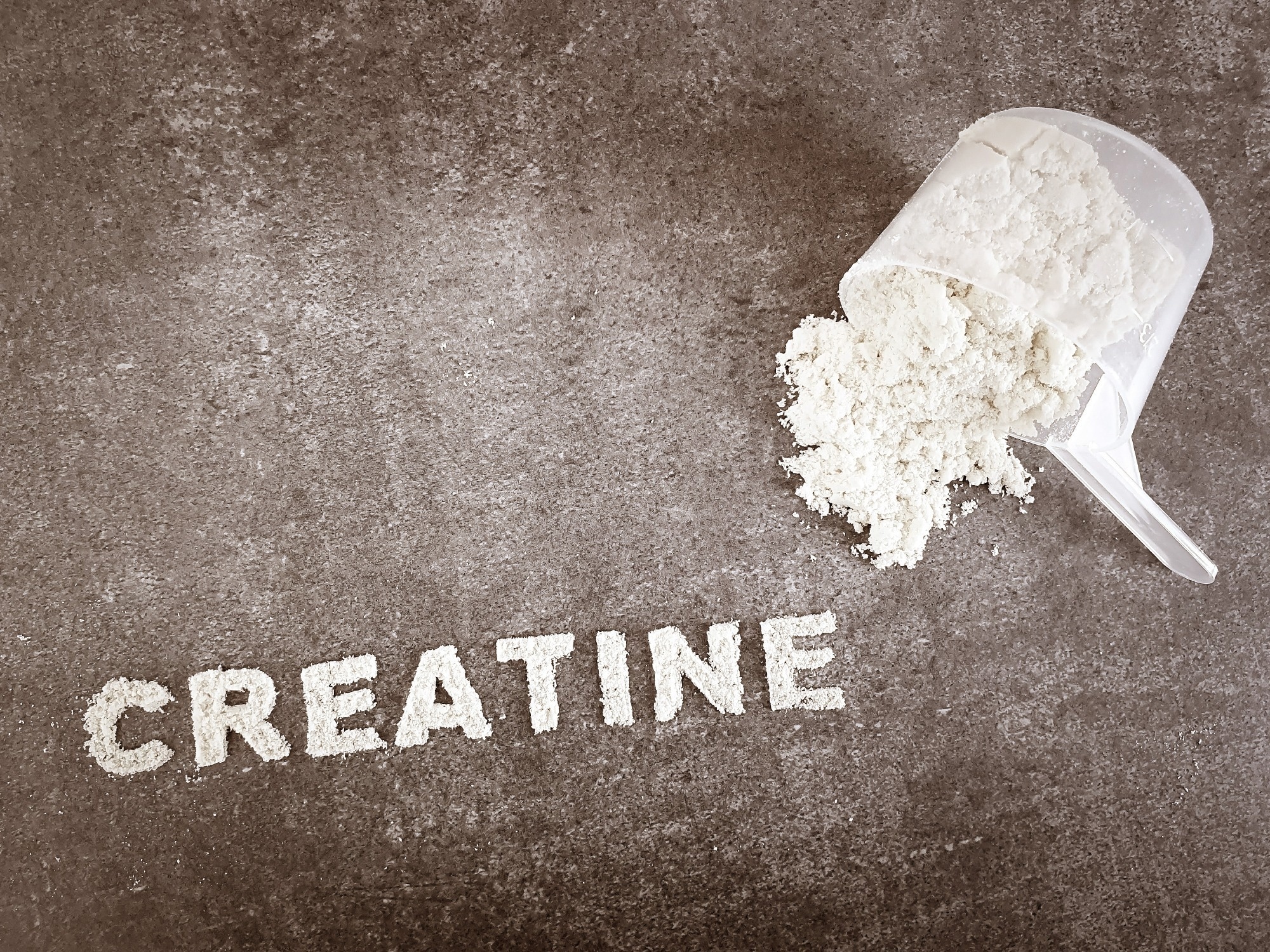 Creatine powder text font on grey stone background with plastic spoon cup