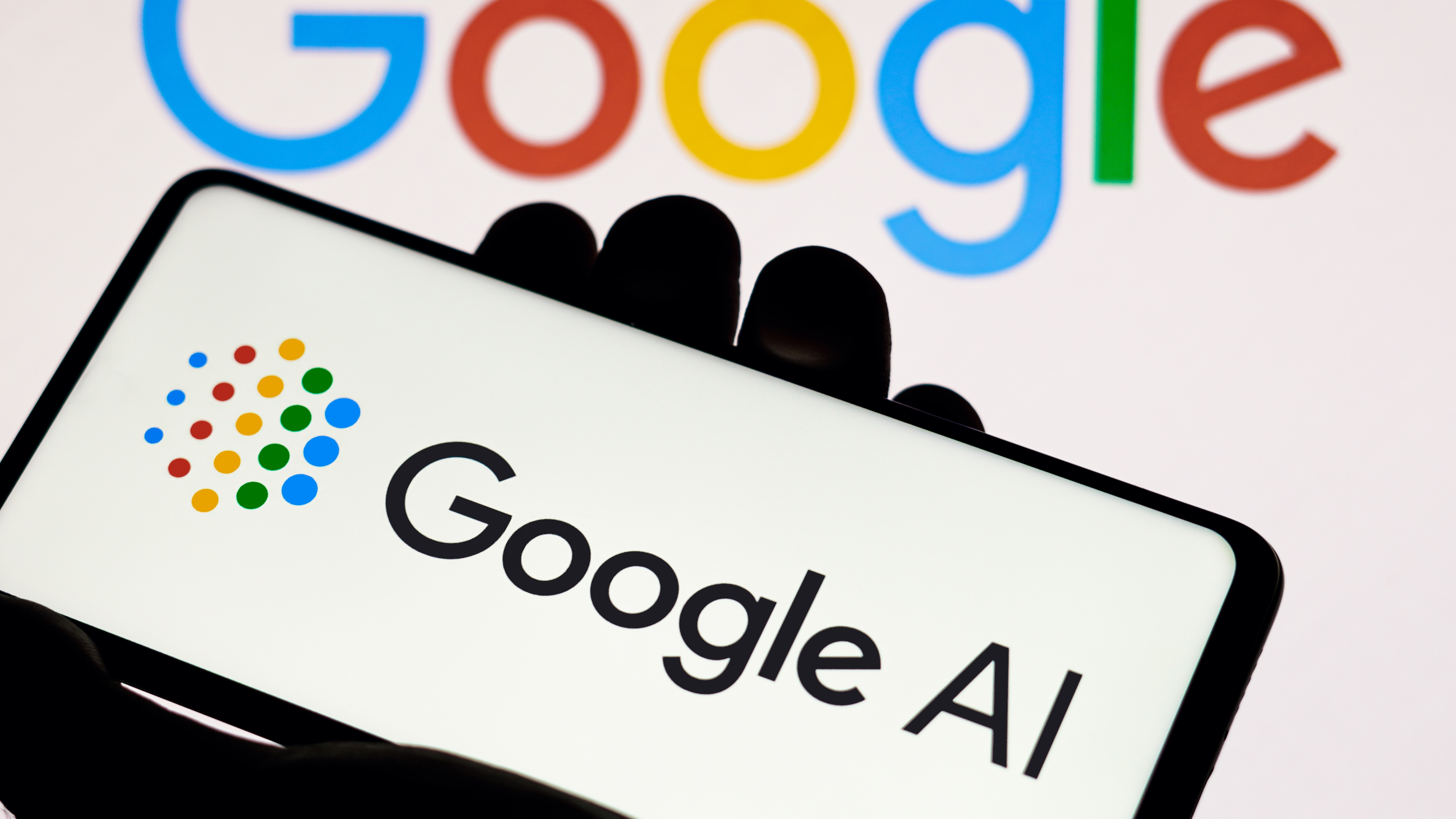 לוגו של Google AI נמצא בטלפון המוחזק ביד, מול לוגו של גוגל