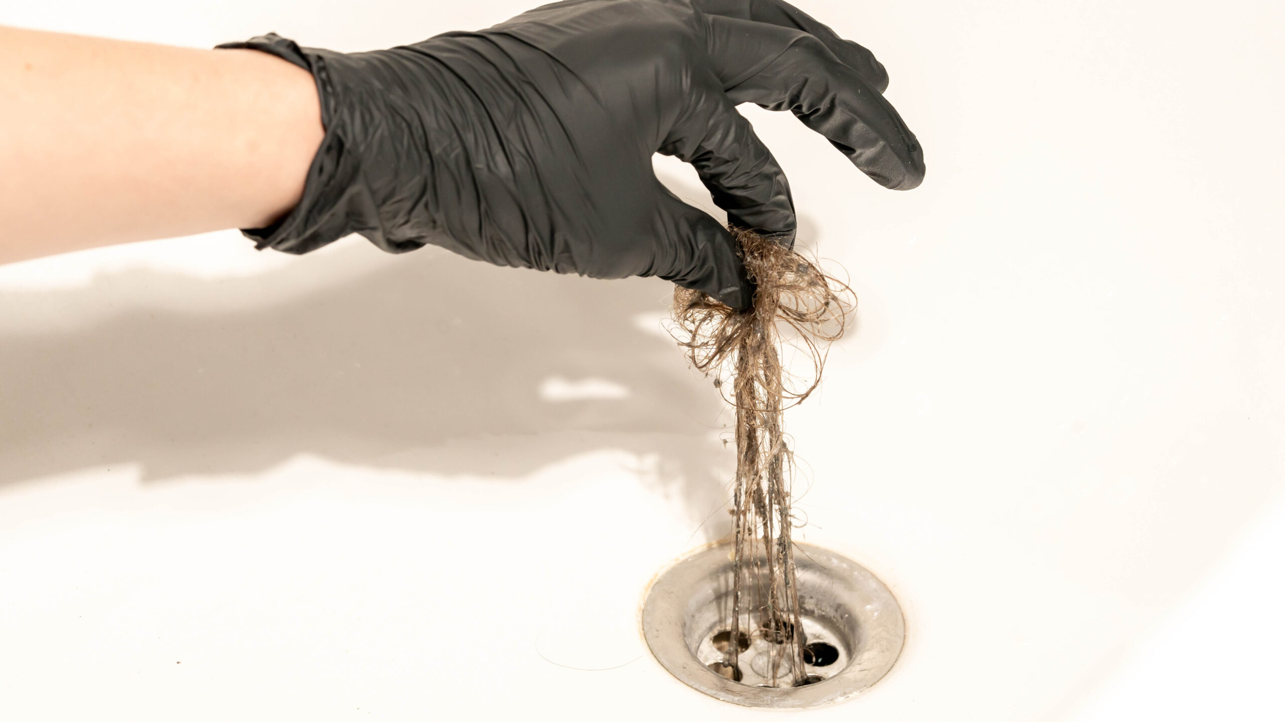 Shower drain being unclogged with a gloved hand