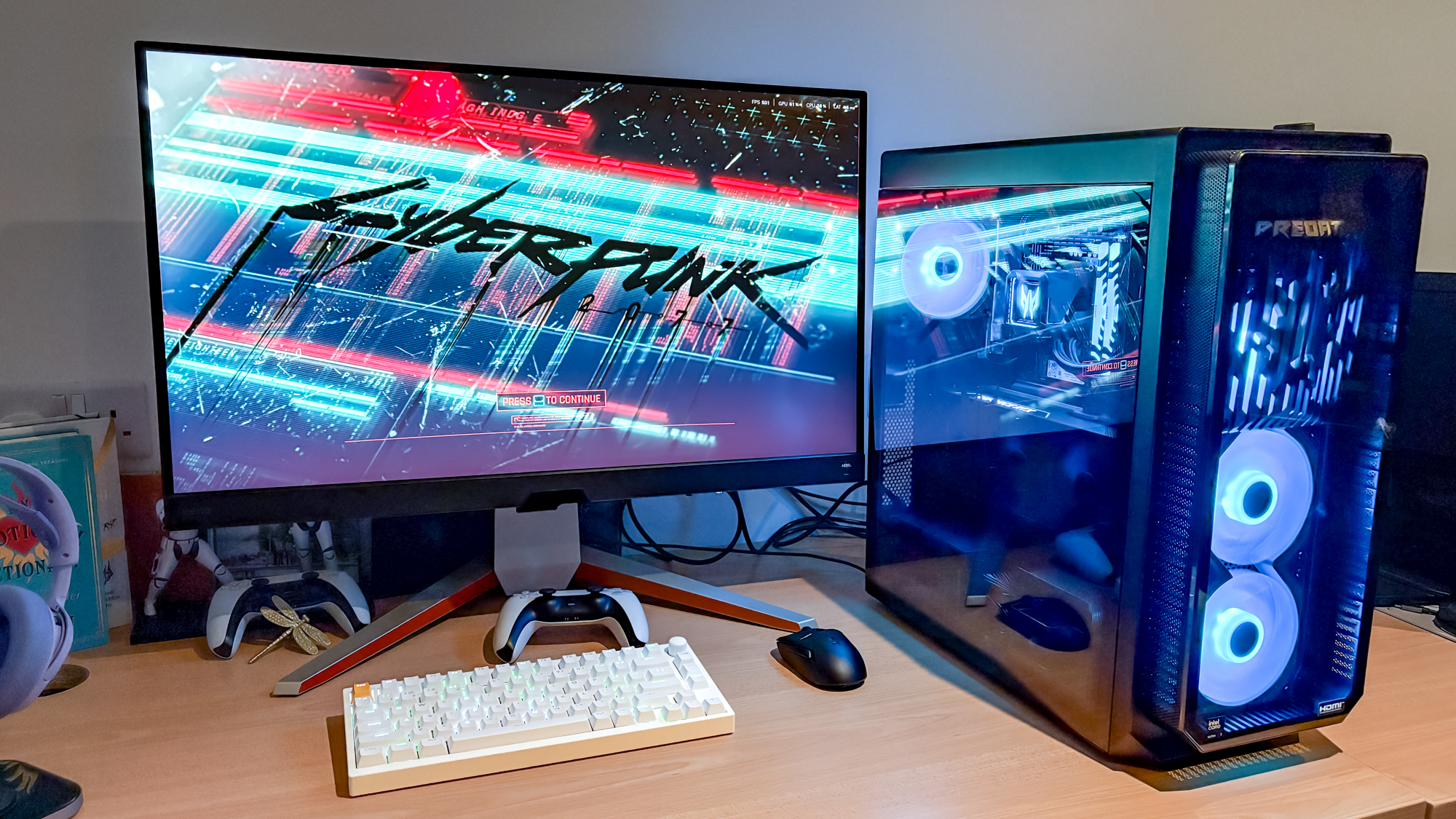Acer Predator Orion 7000 על השולחן עם צג, מקלדת, עכבר ובקר PS5 לידו עם Cyberpunk 2077 בפעולה