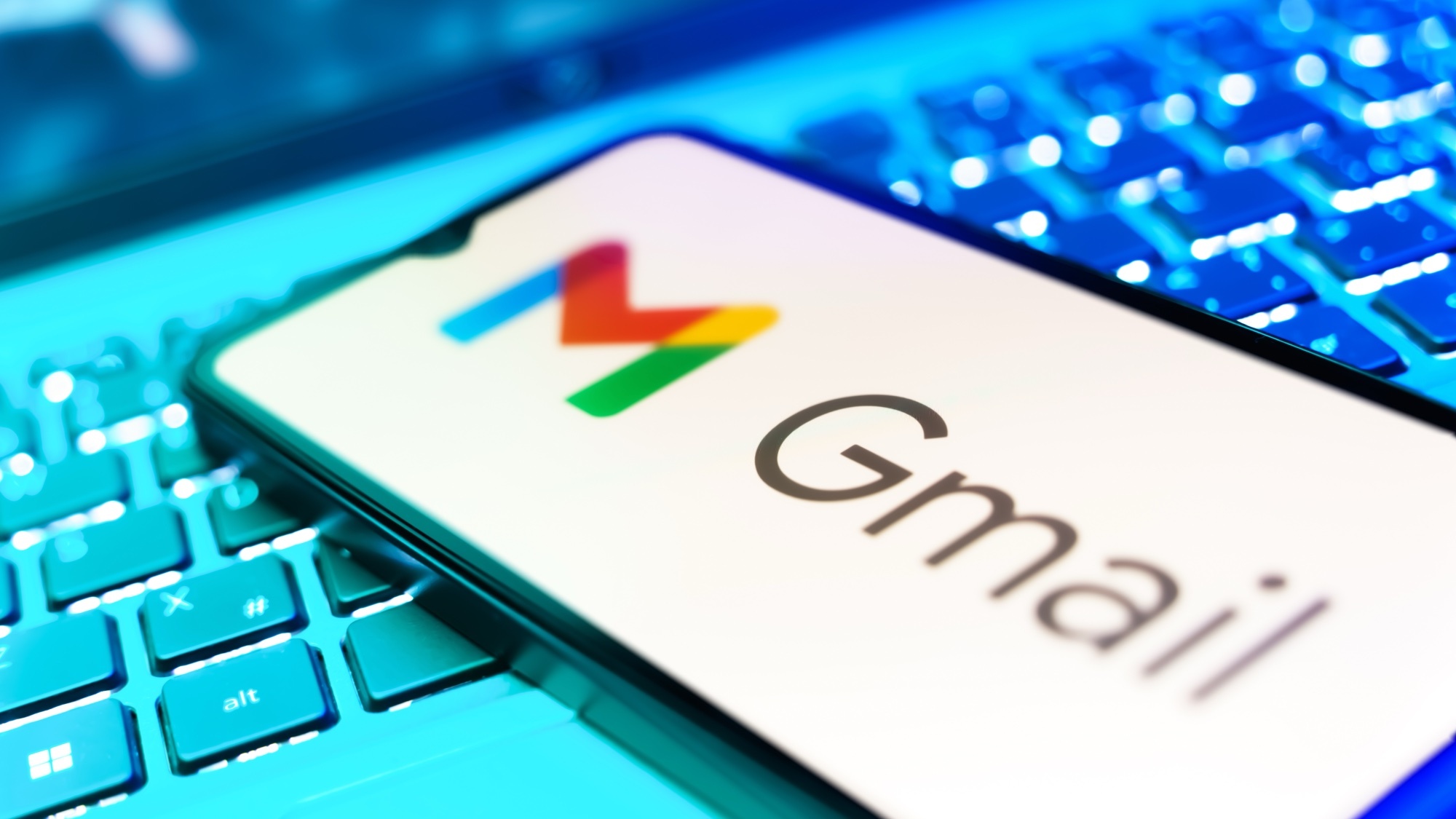 סמארטפון עם הלוגו של Gmail עליו מונח על גבי מקלדת מחשב.