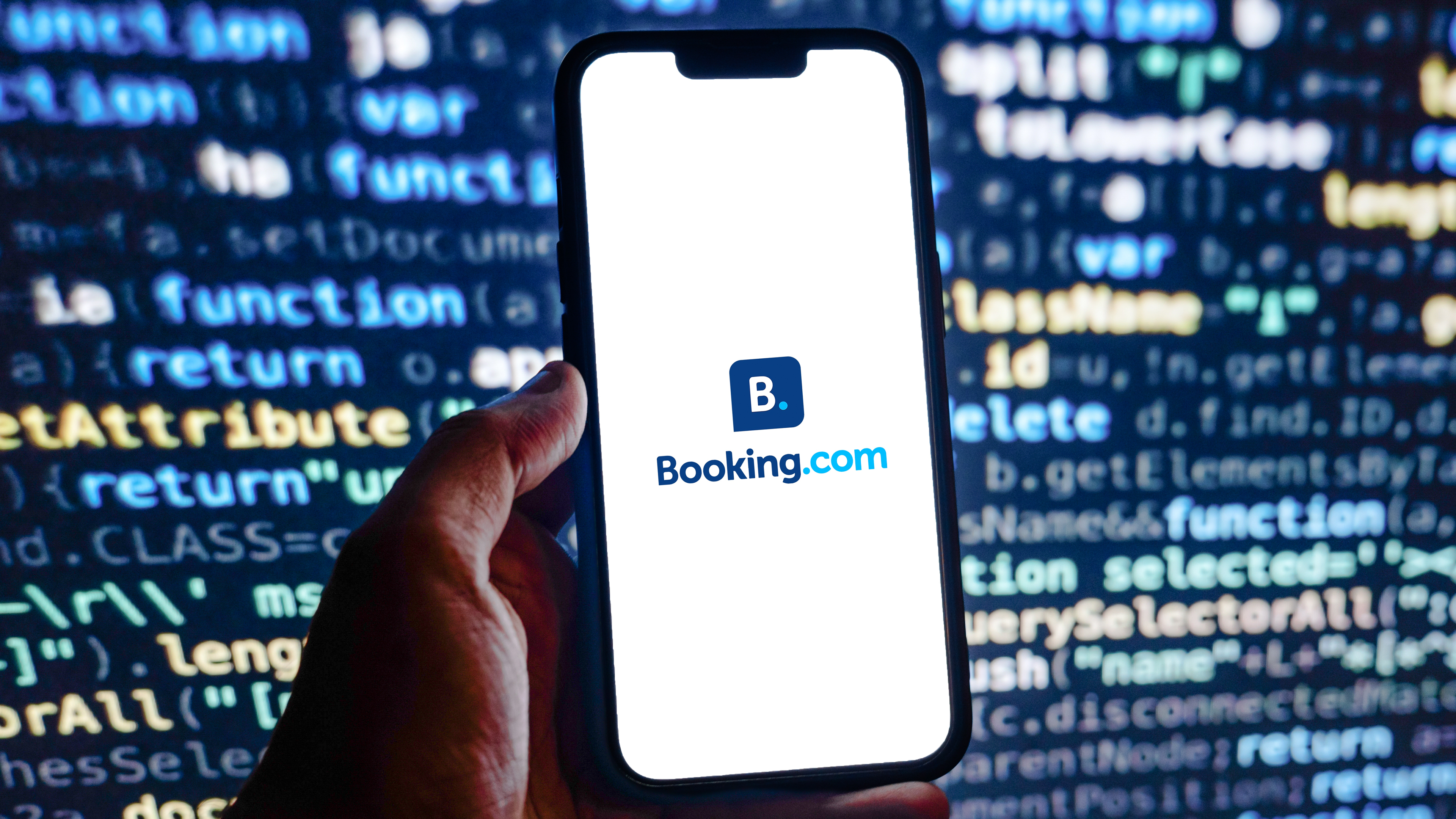 לוגו Booking.com בסמארטפון מול מסך קוד מחשב