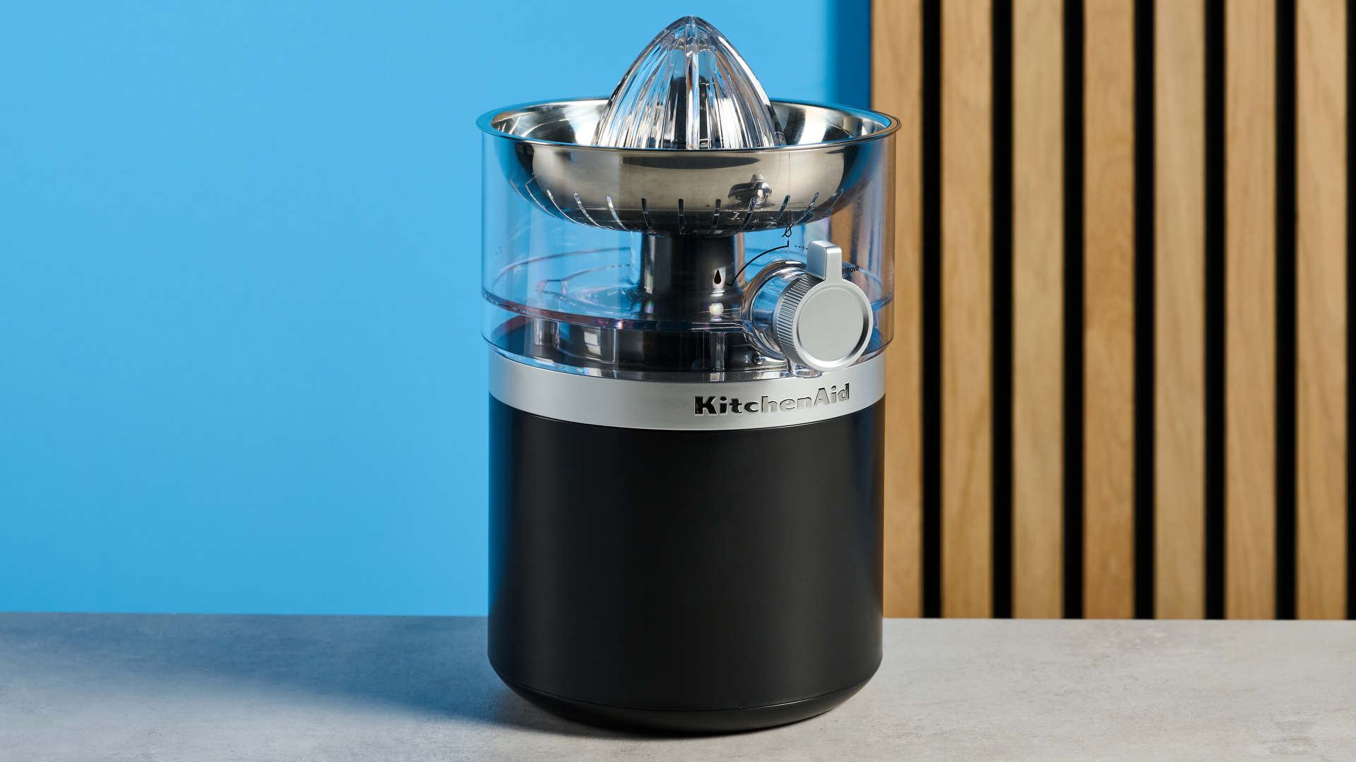 KitchenAid Go מסחטת הדרים חסרת אלחוט בשחור מט שצולם מול רקע כחול.