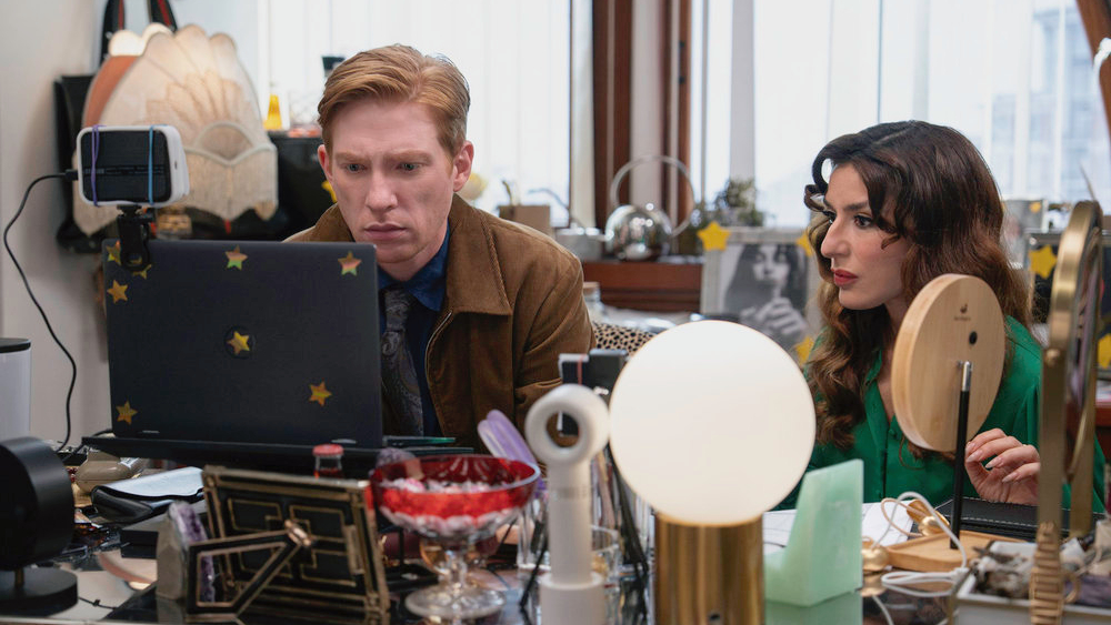 L-R: Ned (Domhnall Gleeson) and Esmeralda (Sabrina Impacciatore) sitting at a computer desk in a scene from "The Paper"