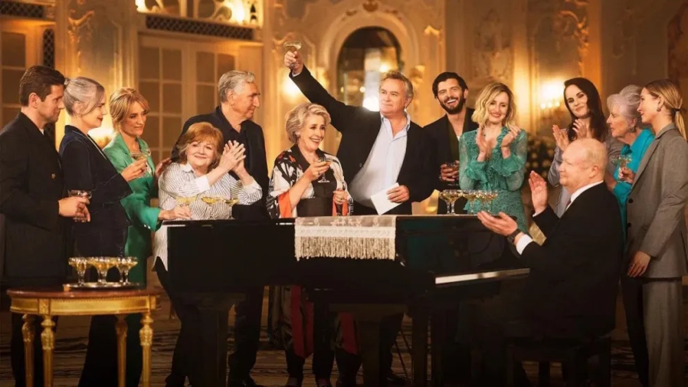 The cast of "Downton Abbey" standing around a grand piano and celebrating in a promotional shot for "Downton Abbey Celebrates the Grand Finale"