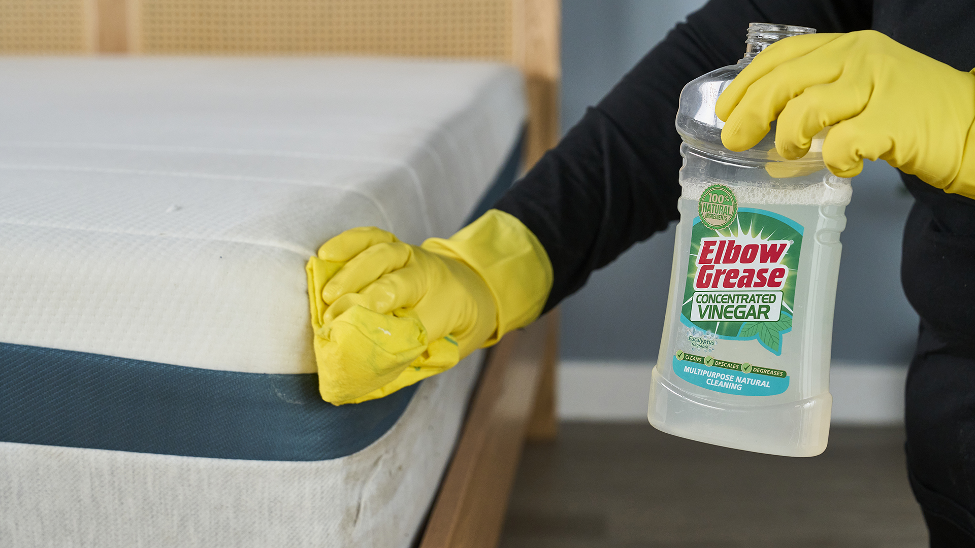 אישה משתמשת במטלית לניקוי מזרון כשהיא מחזיקה בקבוק חומץ