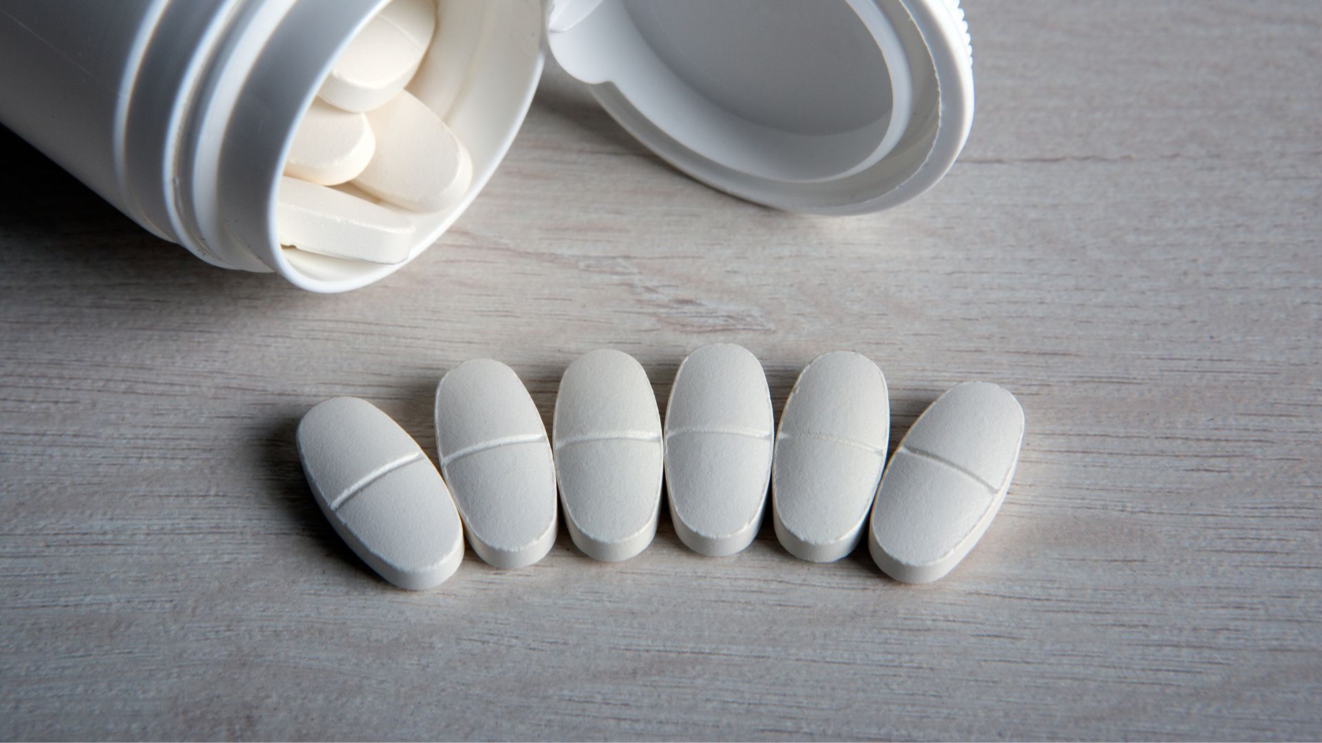 צנצנת פתוחה של תוספי סידן לצד שורה של שש טבליות.