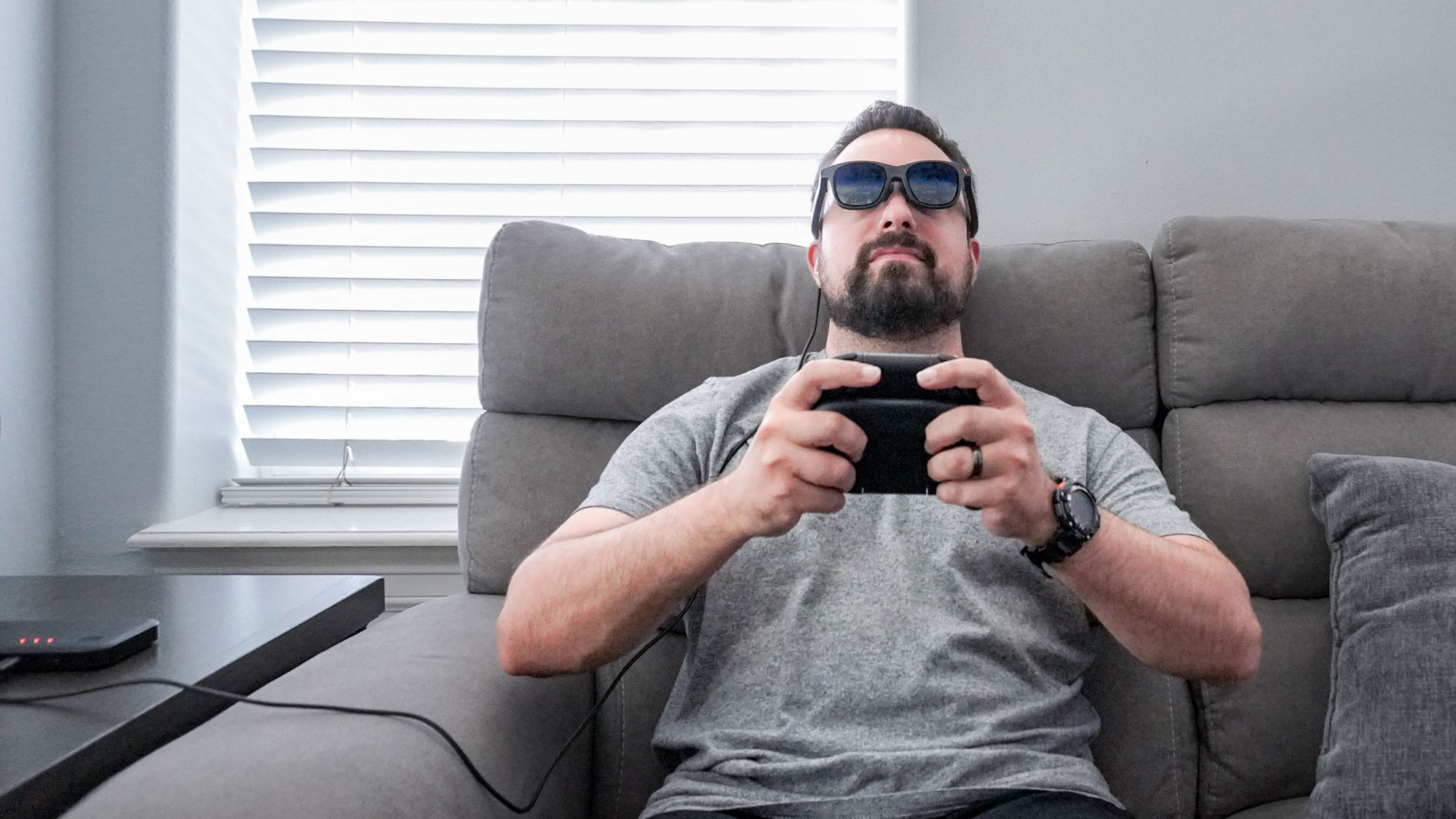אדם שמנגן על Nintendo Switch 2 תוך כדי לבוש משקפי AR על ספה באמצעות המזח הנייד של Viture Pro
