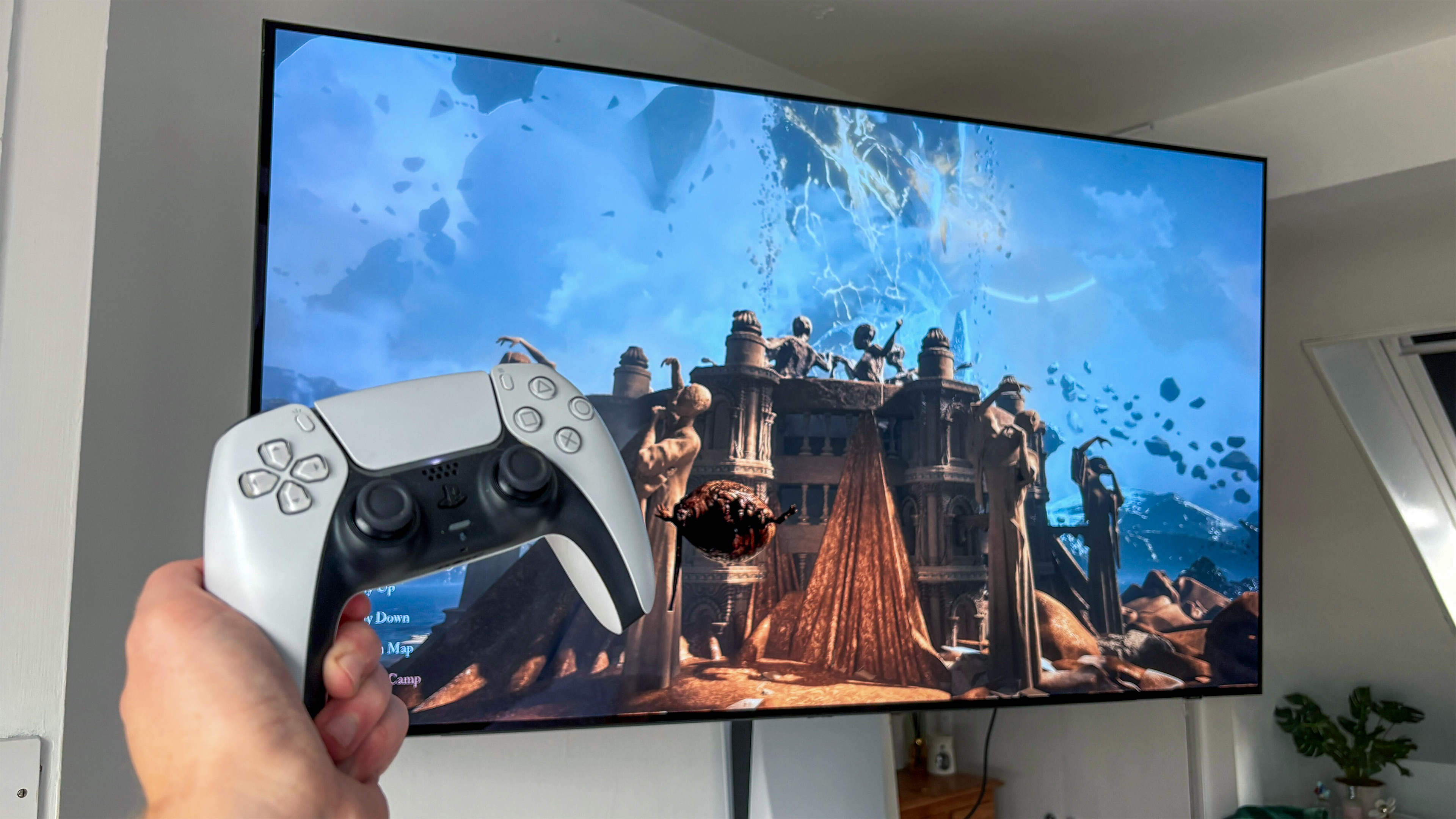 Samsung S90D OLED טלוויזיה מאחורי יד מחזיקה בבקר PS5 DualSense