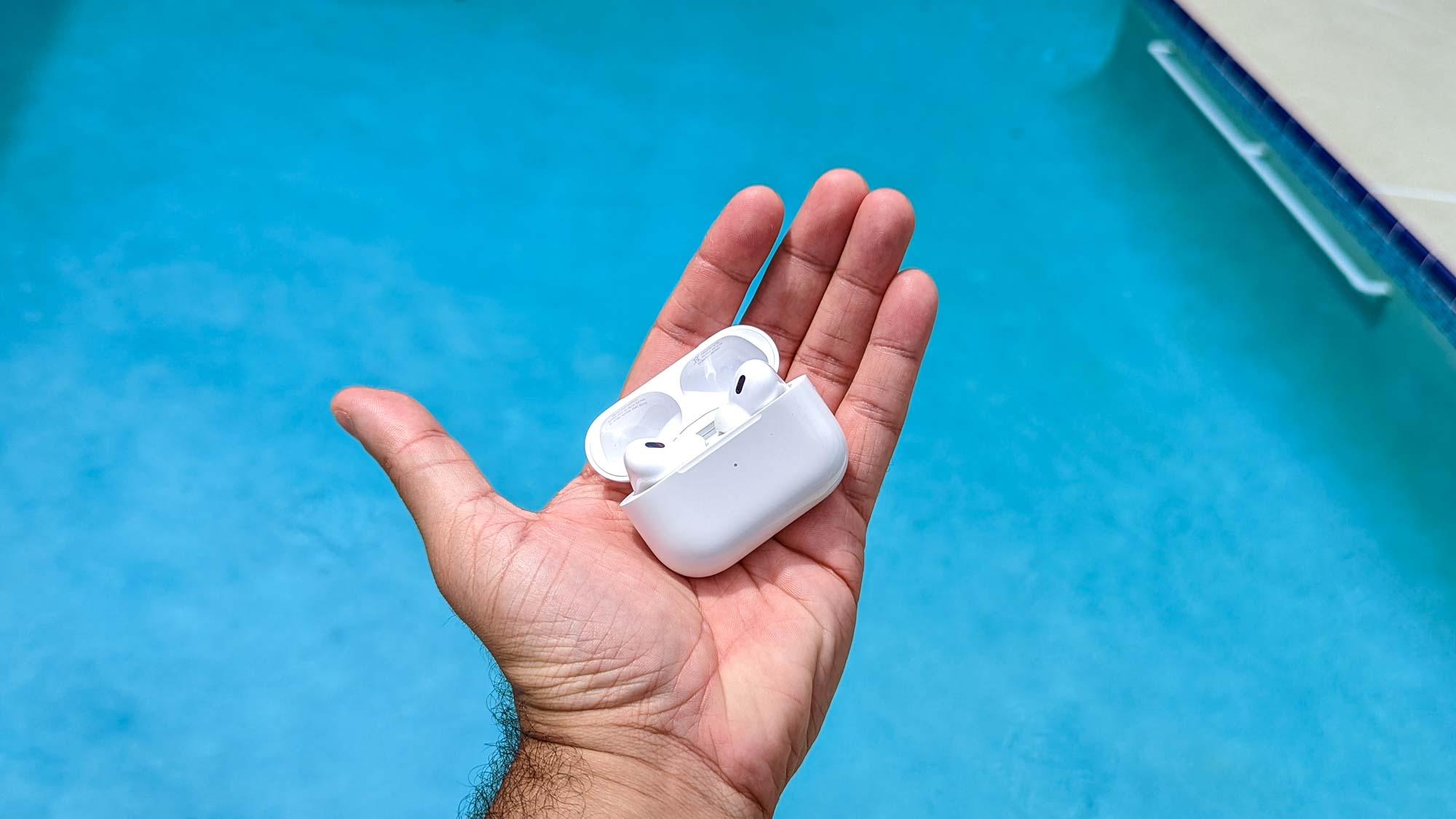 Apple AirPods Pro בתיק טעינה בכף היד של הסוקר ' עם בריכה ברקע