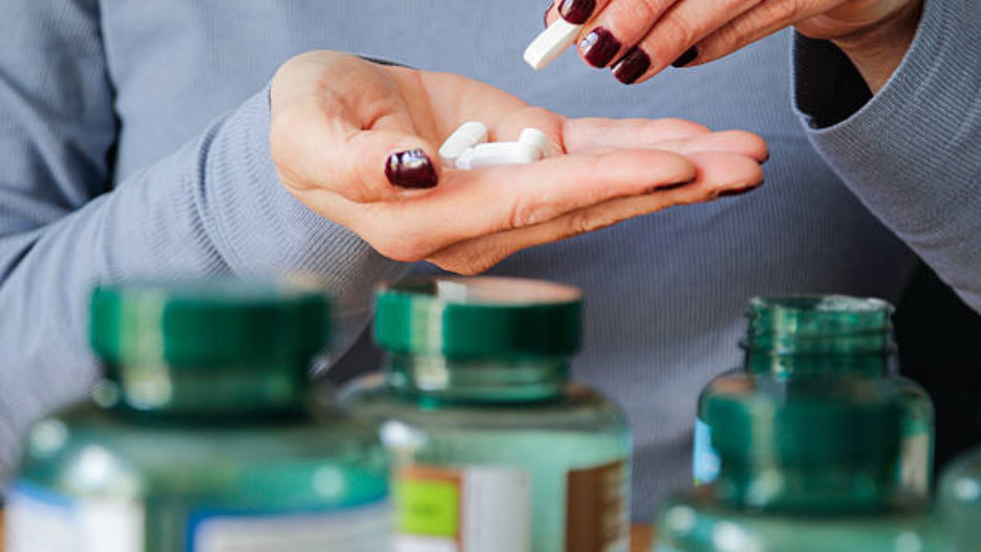 יד מטופחת של אישה מחזיקה חופן של תוספי מולטי ויטמין לבנים.