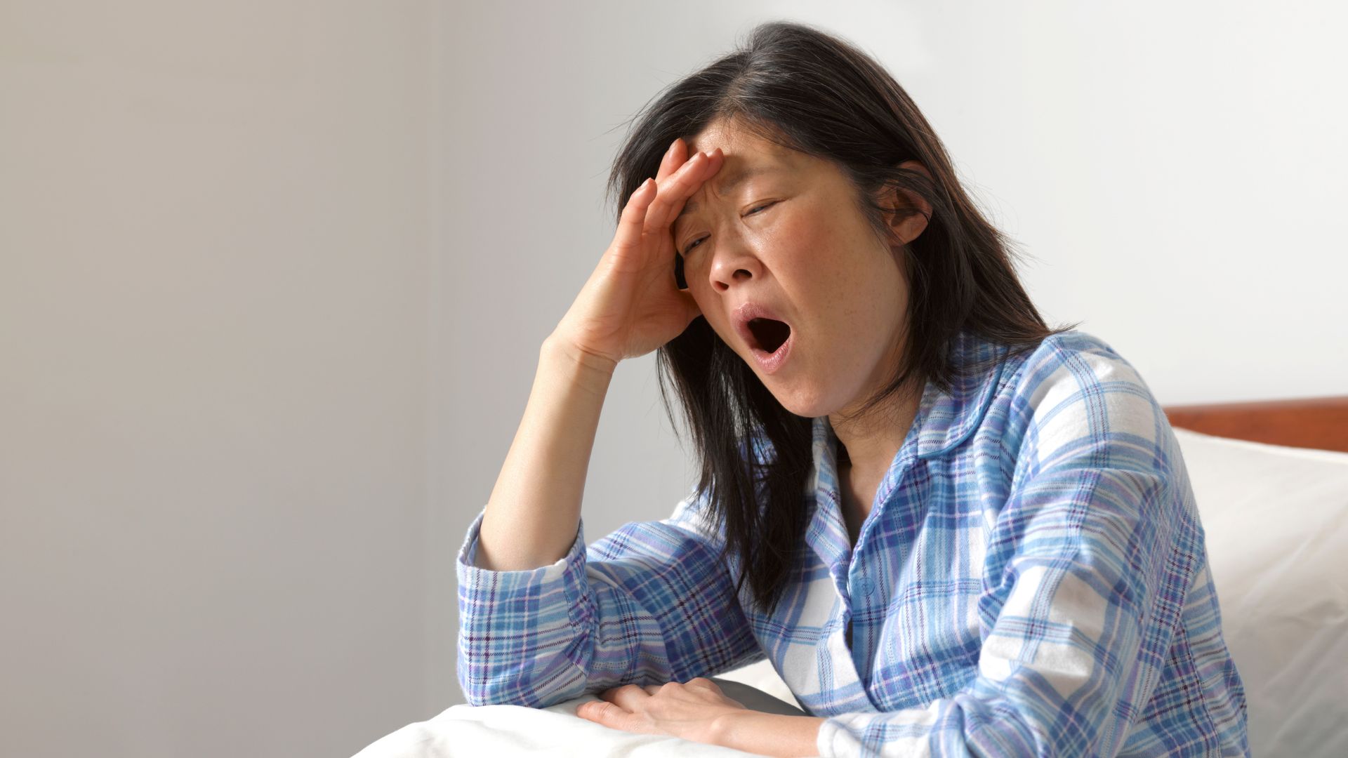 אישה בחולצת פיג'מה כחולה ולבנה יושבת בפה פיהוק.