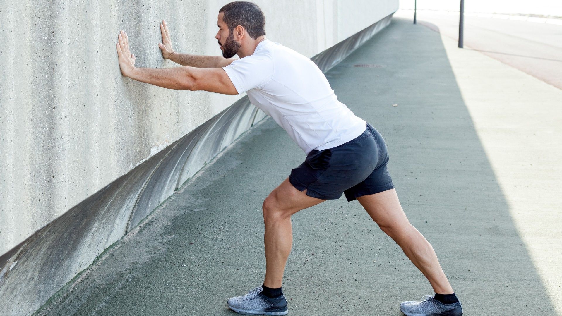 Man with arms pressed on a wall left leg forward and right leg back in a high lunge