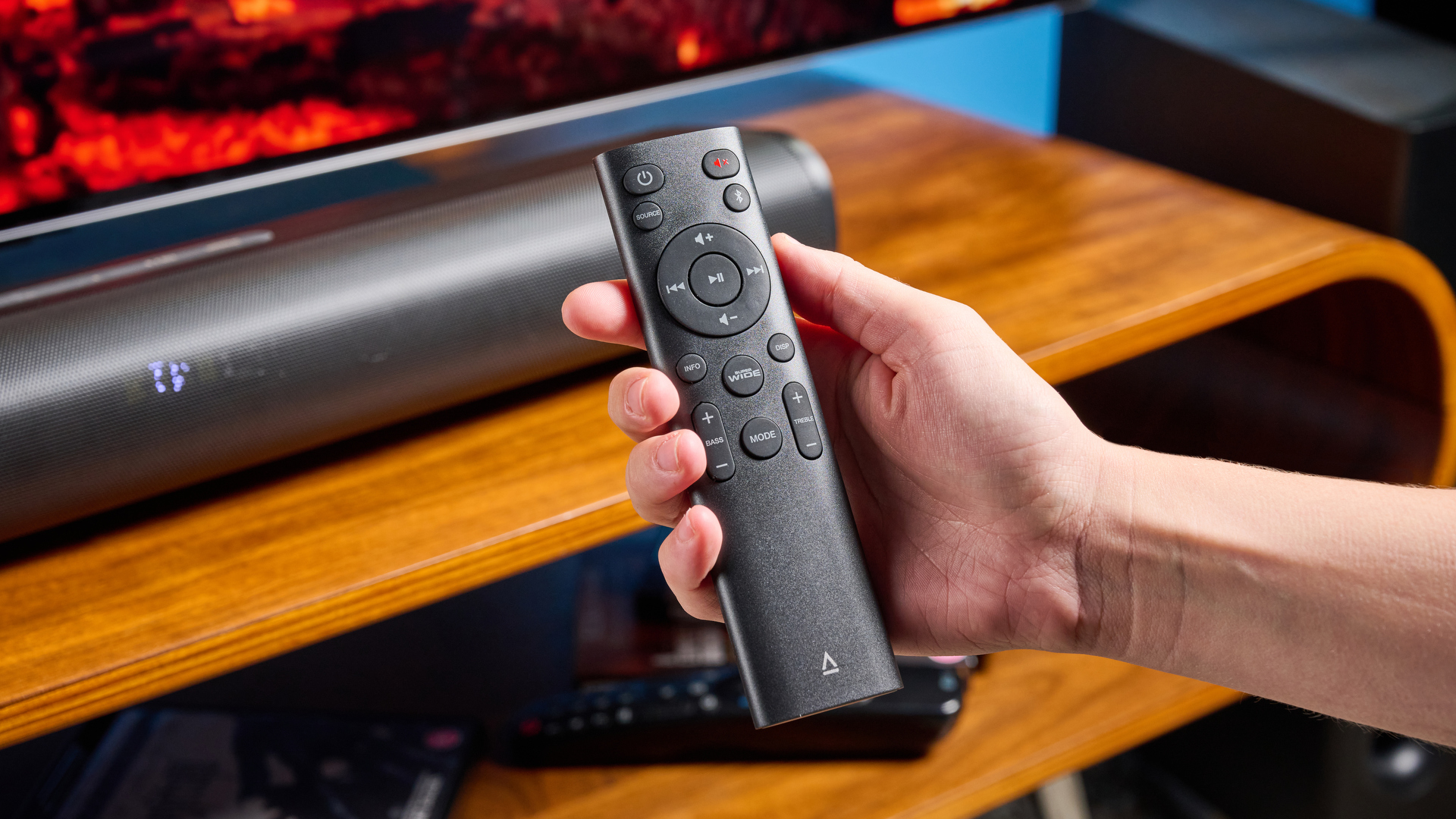 סרגל הסאונד והסאבוופר היצירתי של stage pro, מערכת קולנוע ביתי בתקציב סופר-תקציבי עם 2.1 ערוצים ושלט רחוק מצולם על מעמד טלוויזיה מעץ עם טלוויזיה מאחור