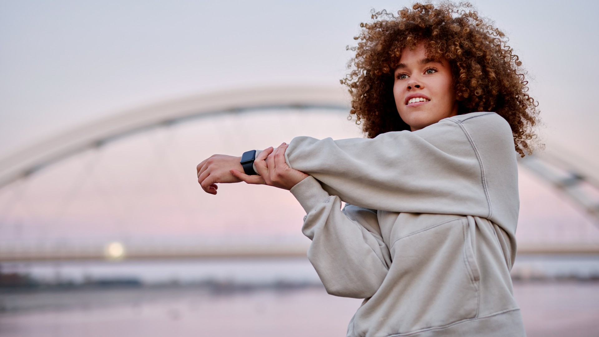 אישה עומדת בחוץ בשקיעה מותחת את זרועה על גופה