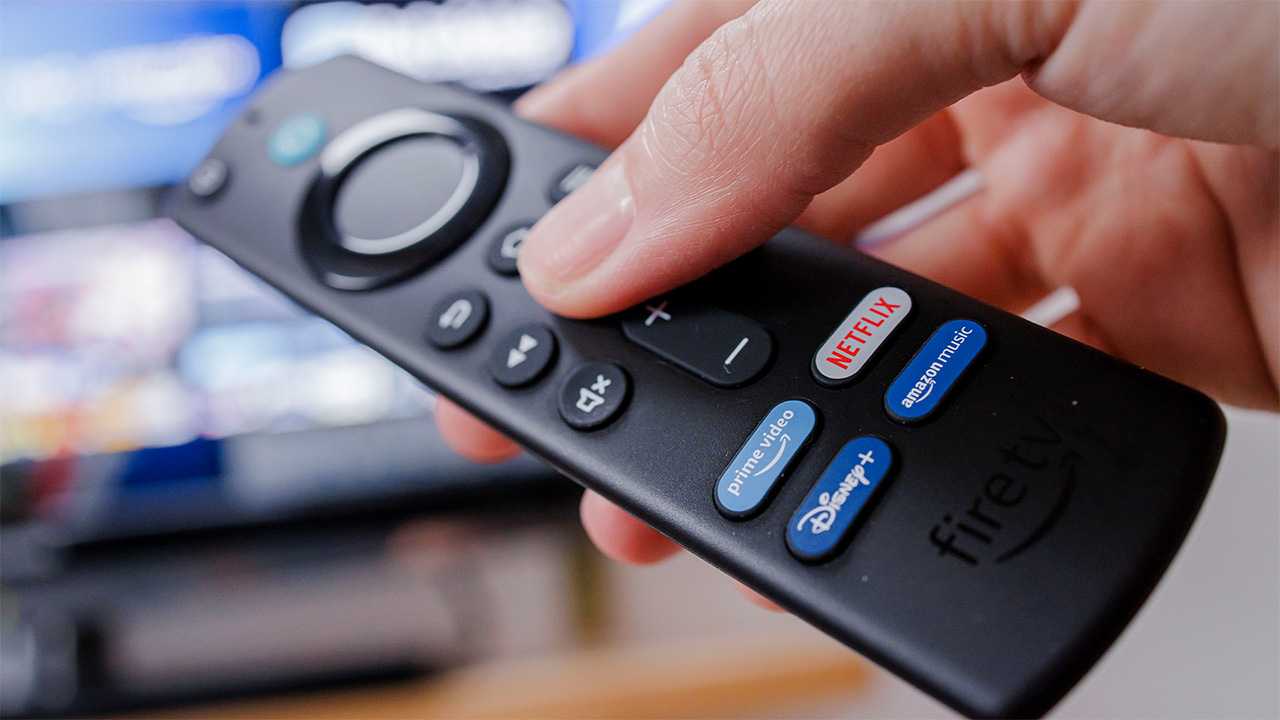 אדם מחזיק ב- Amazon Fire Stick עם טלוויזיה ברקע