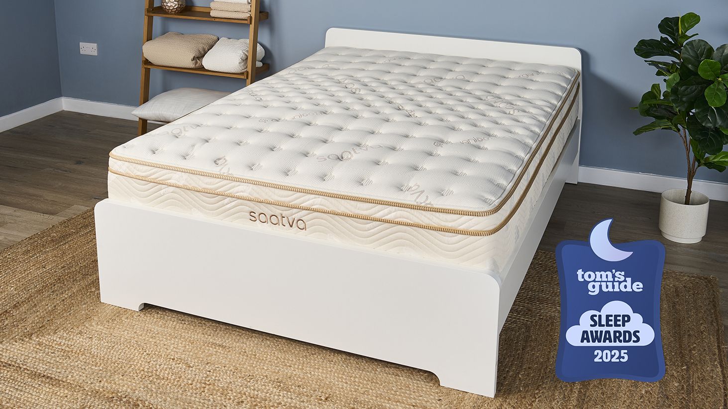 The Saatva Classic Luxury Innerspring Hybrid Mattress, our Tom's Guide Sleep Awards Mattress of The Year Winner for 2025, is shown here on a white wooden bed frame, photographed in our blue Sleep Product Testing Lab during our most recent full cover to base retesting completed just last month