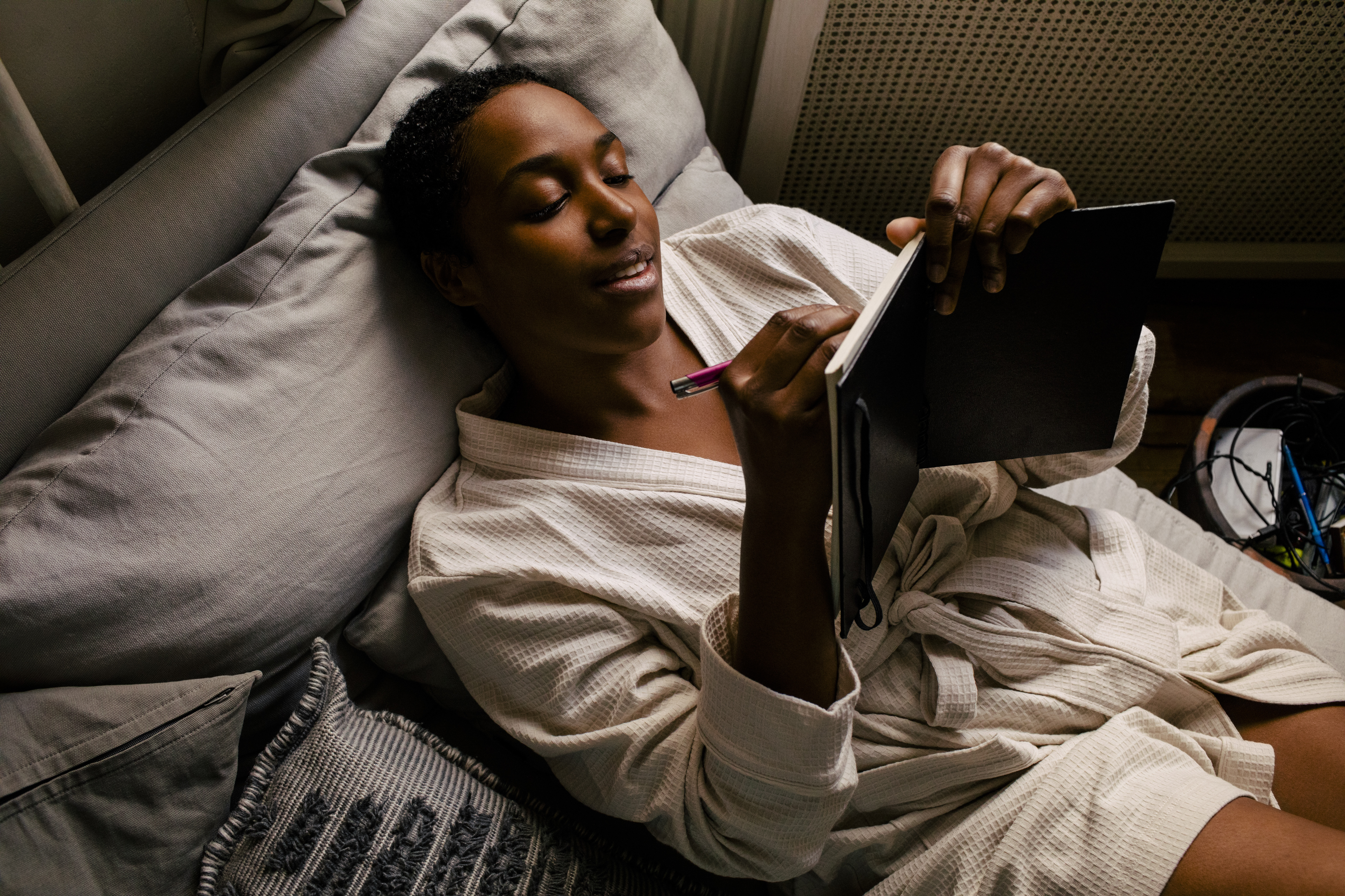 אישה שוכבת במיטה לבושה בחלוק כשהיא כותבת ביומן.