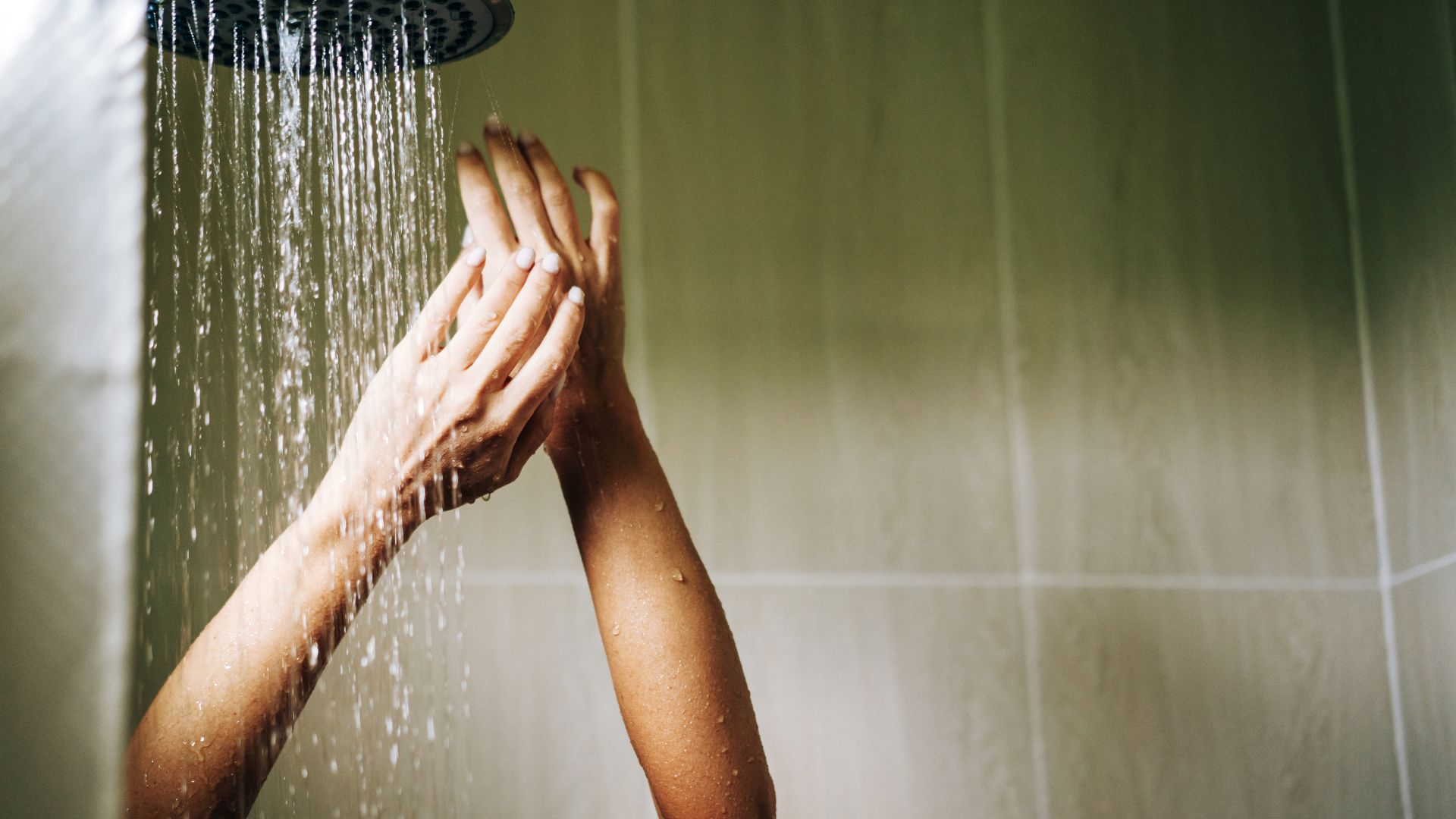 אדם עומד במקלחת עם ידיים מורמות. חדר הרחצה כולל חיפוי אפקט עץ בהיר על הקיר.