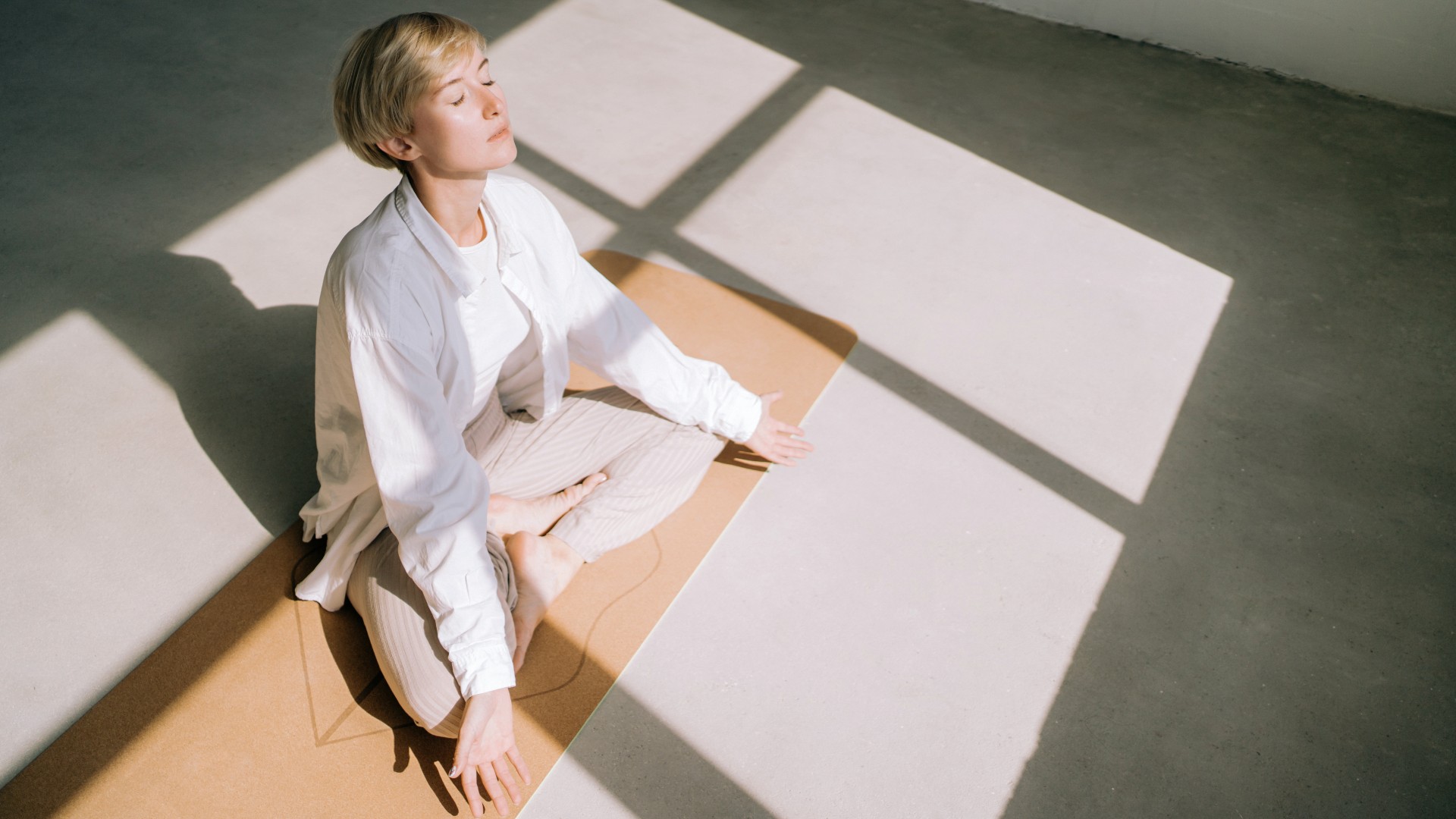 אישה ישבה ברגליים משוכלות על הרצפה וביצעה תרגיל נשימה בעיניים עצומות