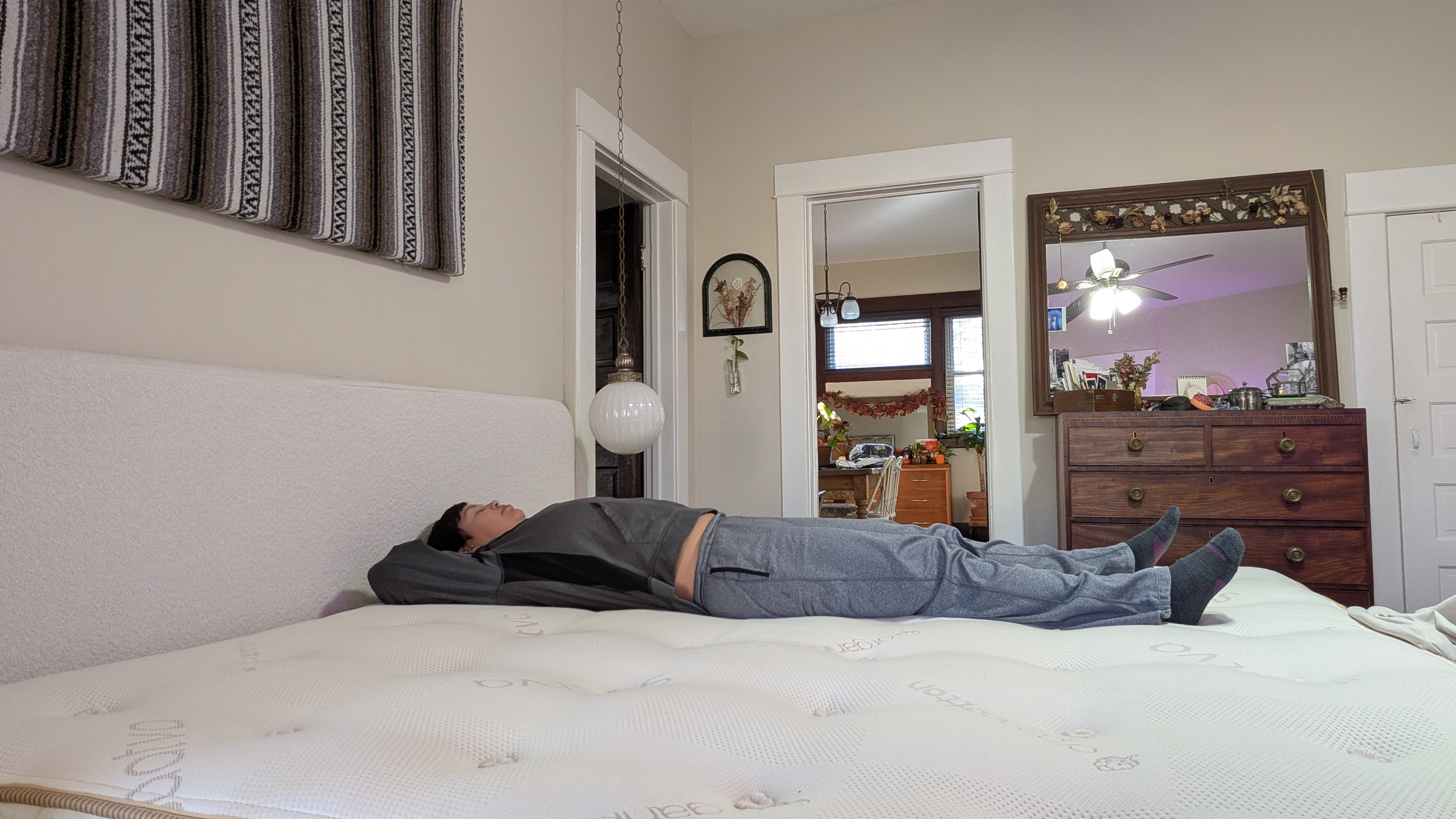 בודק המזרן אלכס מונח על המזרון ההיברידי Saatva Latex כדי להראות את רמת הנוחות והתמיכה שלו