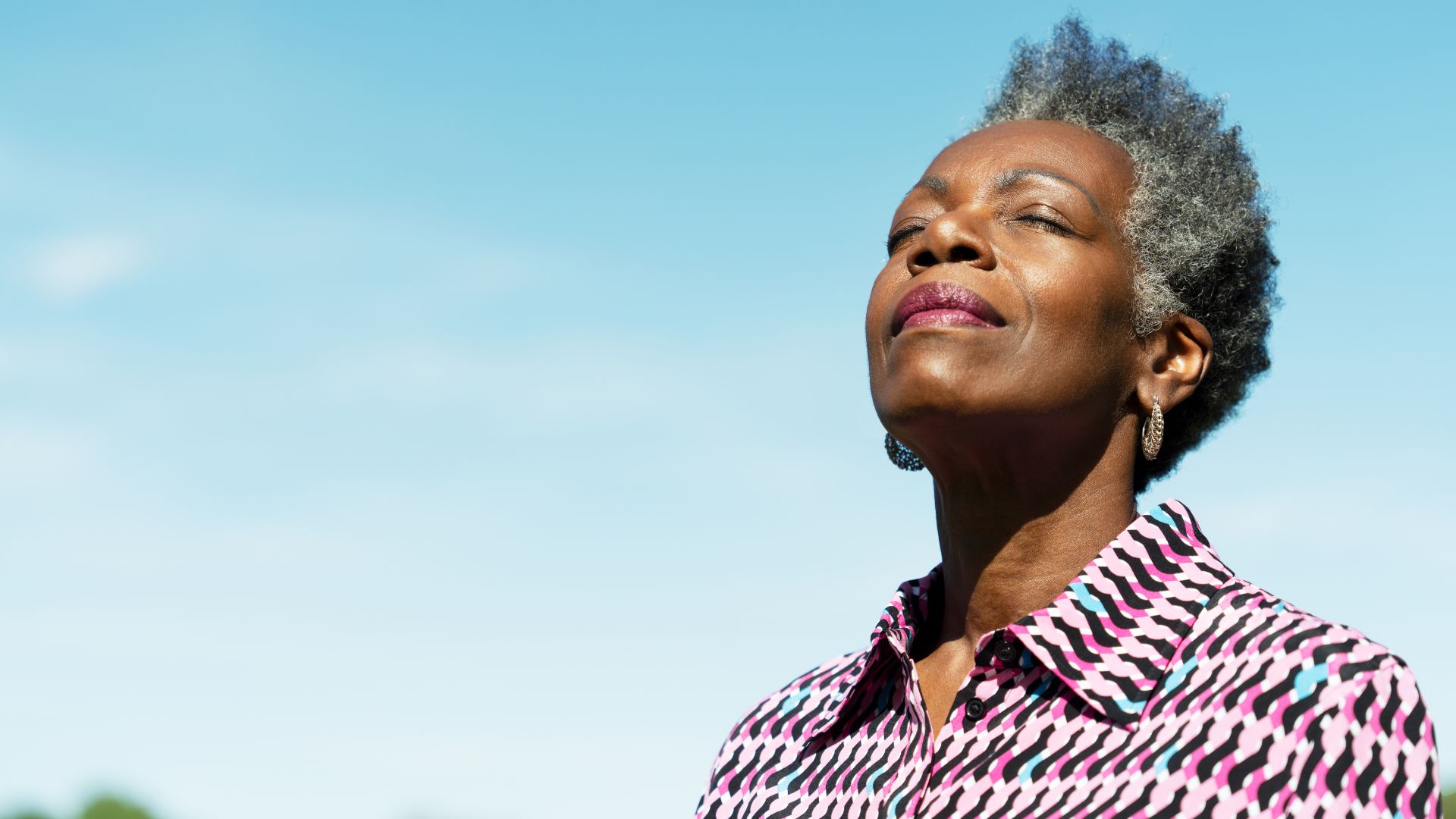 אישה בוגרת חייכנית מתחממת באור השמש של הבוקר.