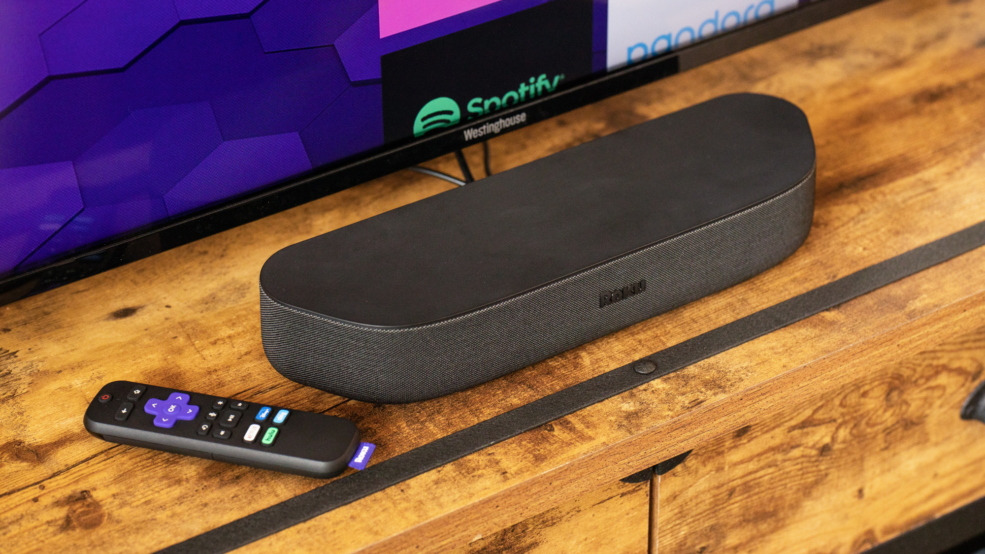 Roku Streambar על דלפק מול טלוויזיה ליד שלט של Roku
