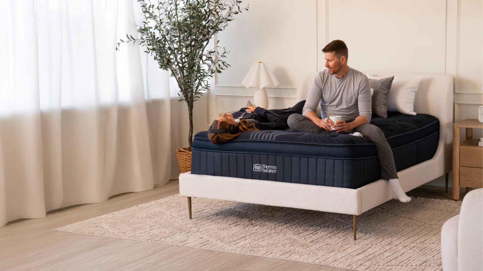 גבר מתיישב על מזרון ה-ThermoBalance כשהוא מחזיק ספל, ואישה עם אוזניות שוכבת בתנוחי שכיבה לידו.