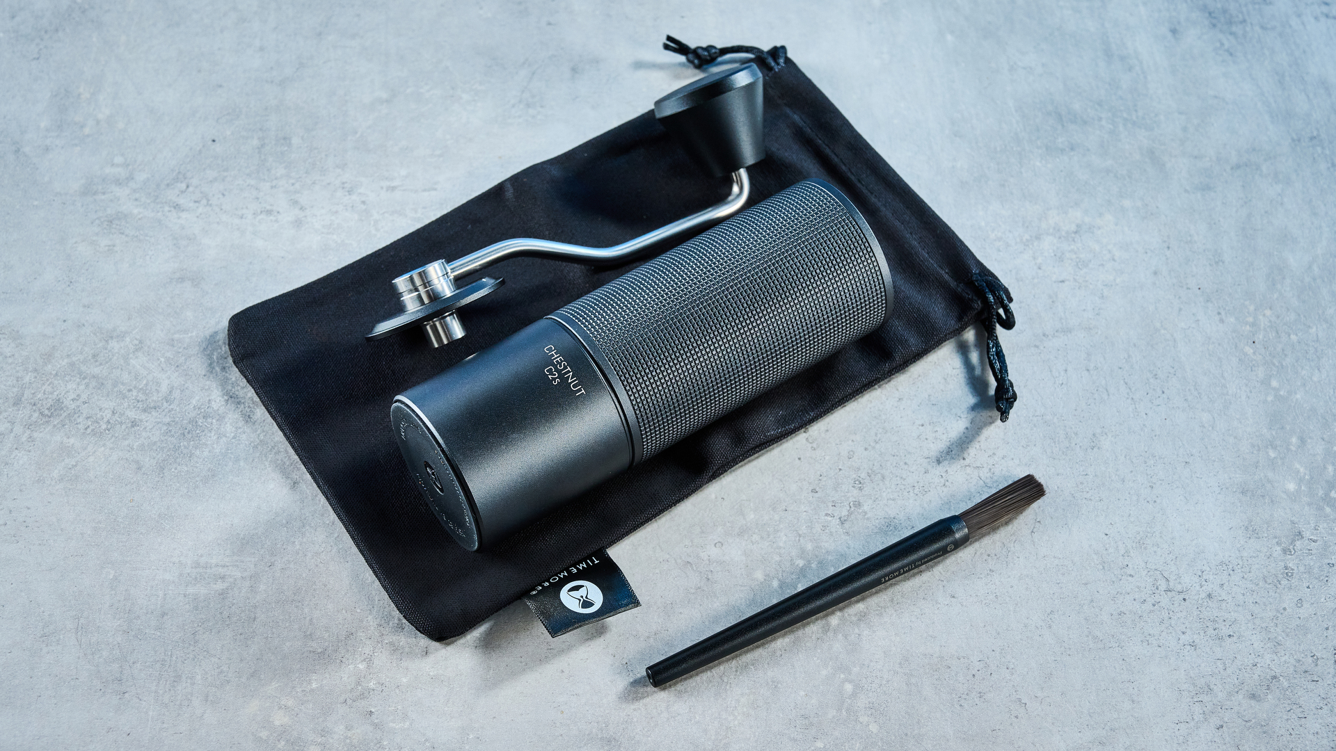 מטחנת הקפה של timemore chestnut c2s בשחור, מציגה את ארכובה היד ואת תא התפיסה שלה שצולמו על רקע המדריך הכחול של Tom's