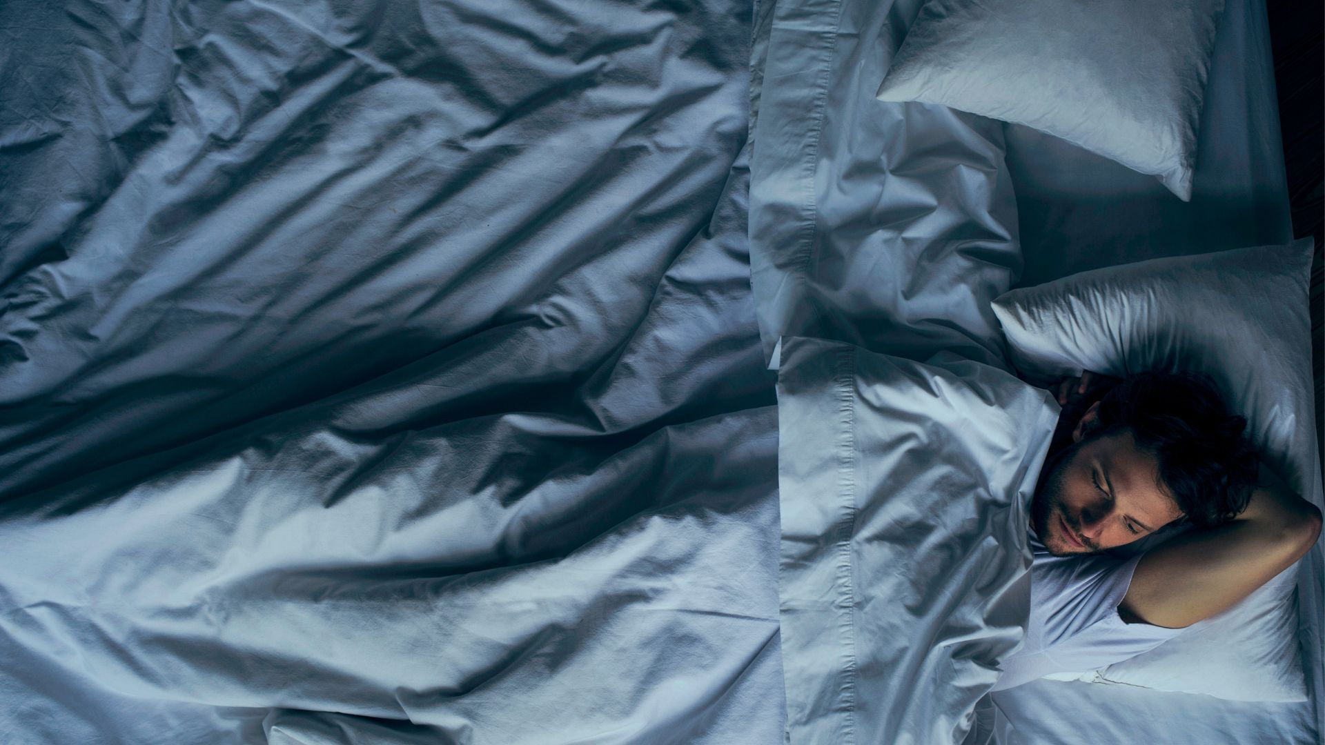 אדם שוכב ער בלילה. הוא שוכב על הגב במיטה עם מצעים לבנים. 