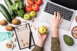 Woman workspace with healthy food. Female hands writing in the notepad words