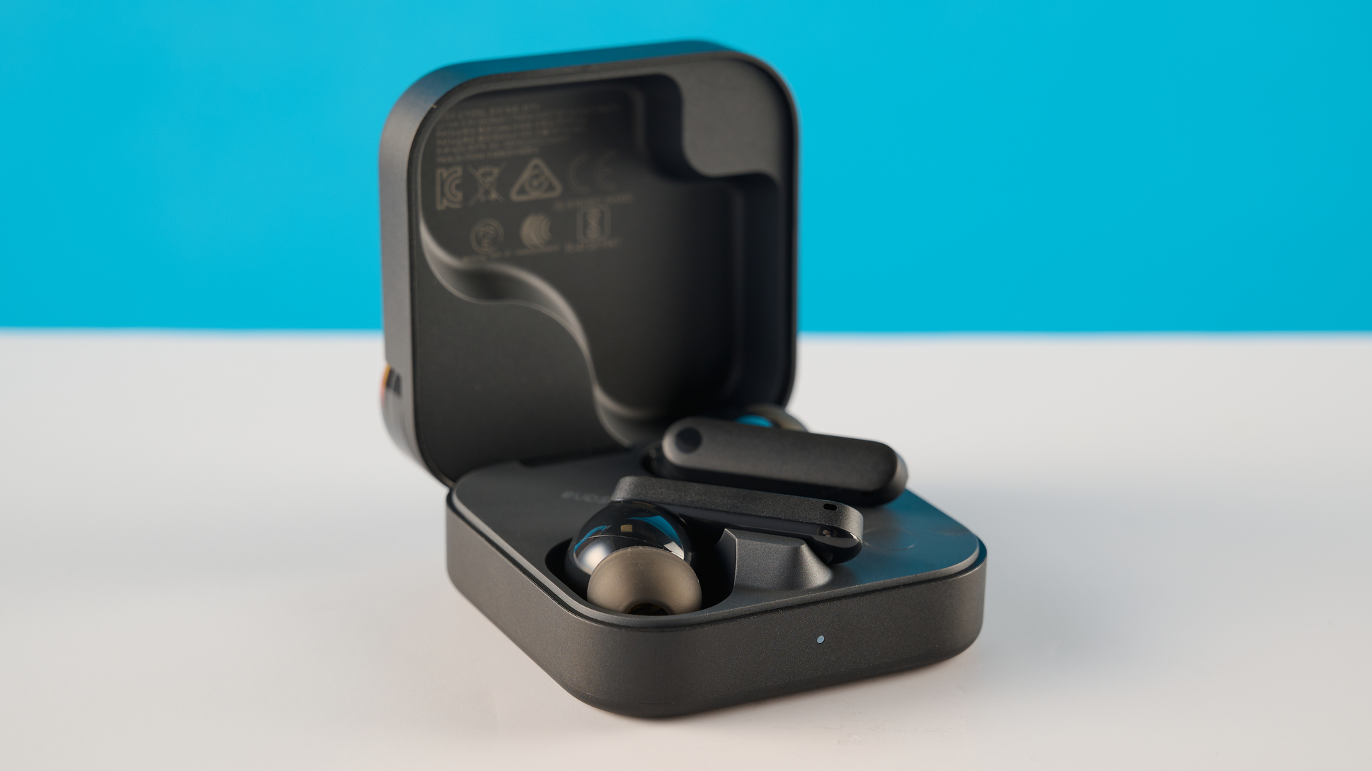 CMF Buds 2 בצילומי אפור כהה על שולחן אפור מול רקע כחול