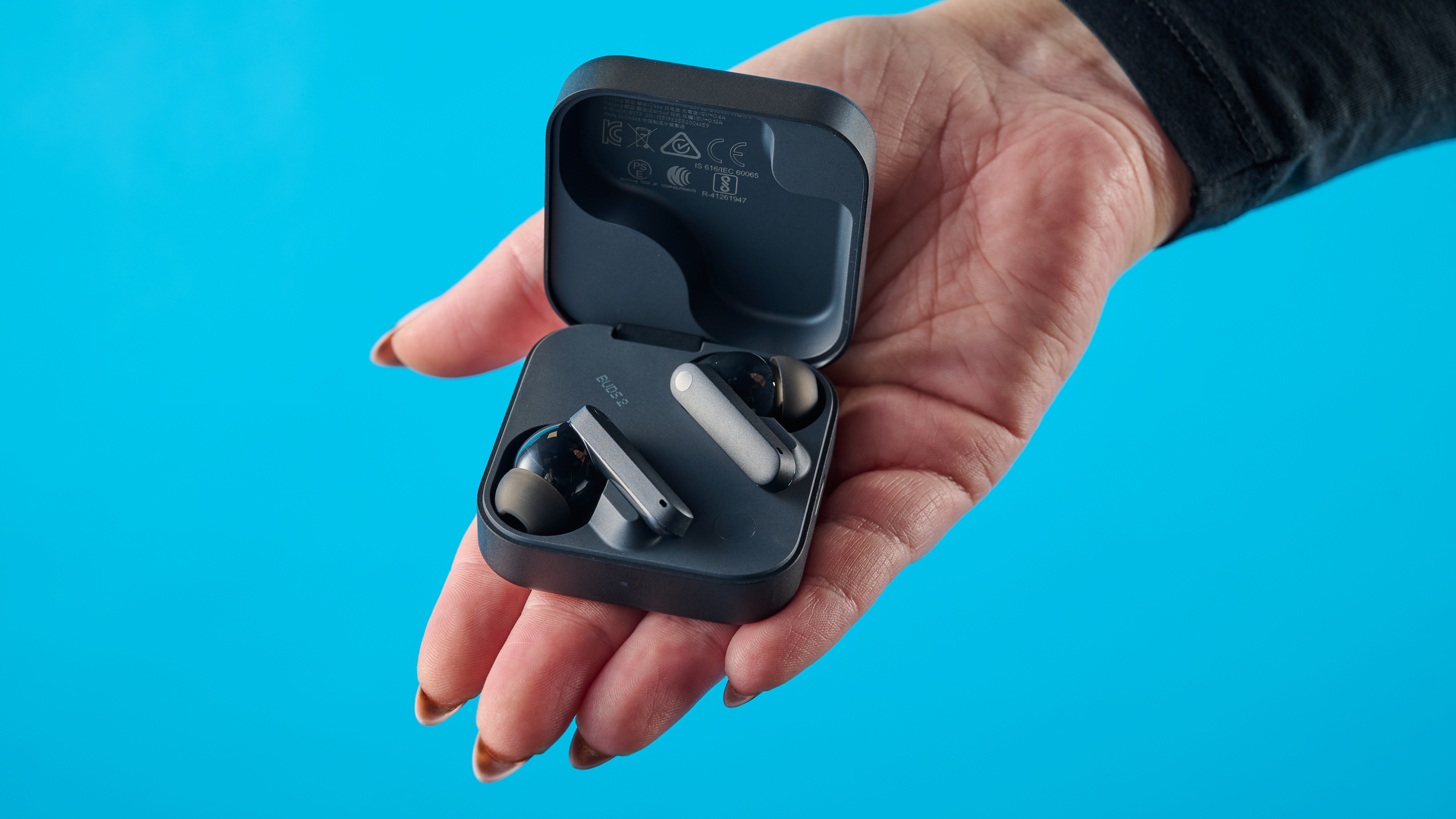 CMF Buds 2 בצילומי אפור כהה על שולחן אפור מול רקע כחול