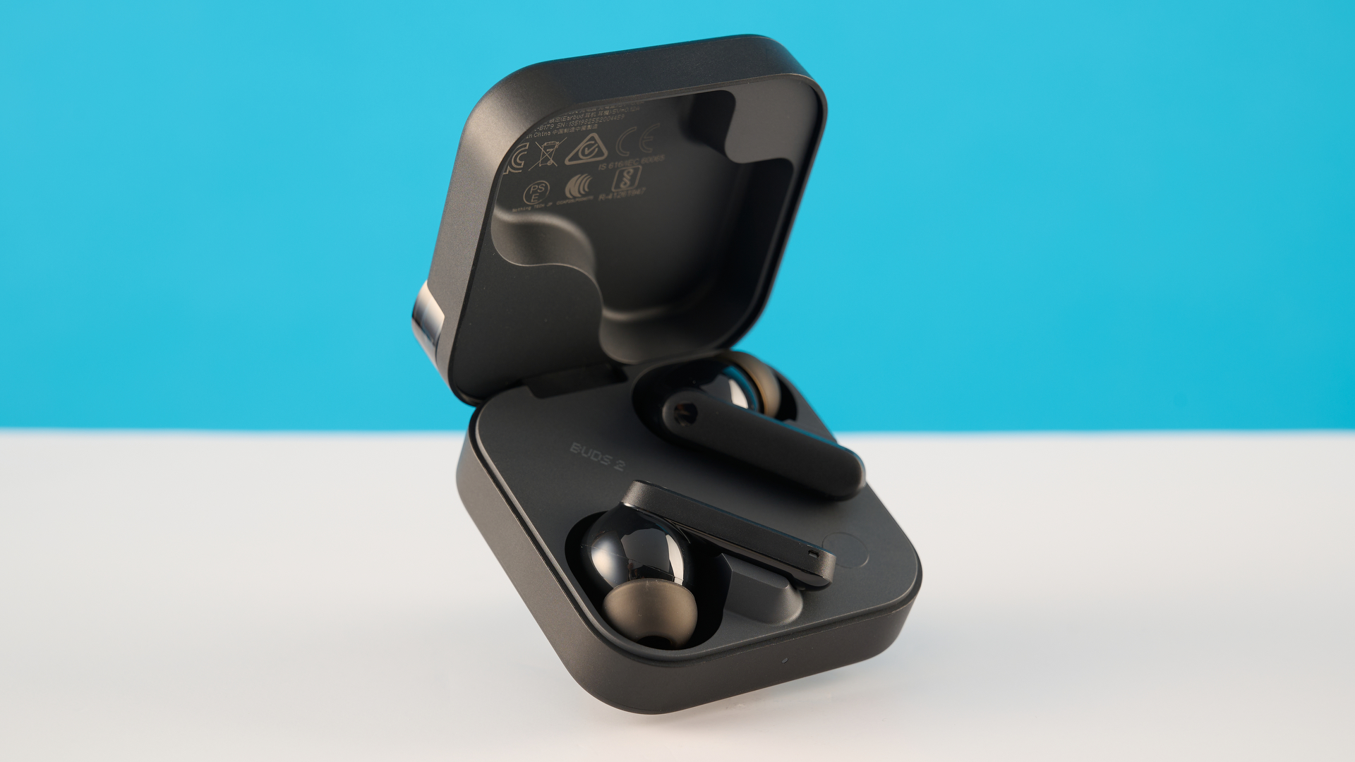 CMF Buds 2 בצילומי אפור כהה על שולחן אפור מול רקע כחול