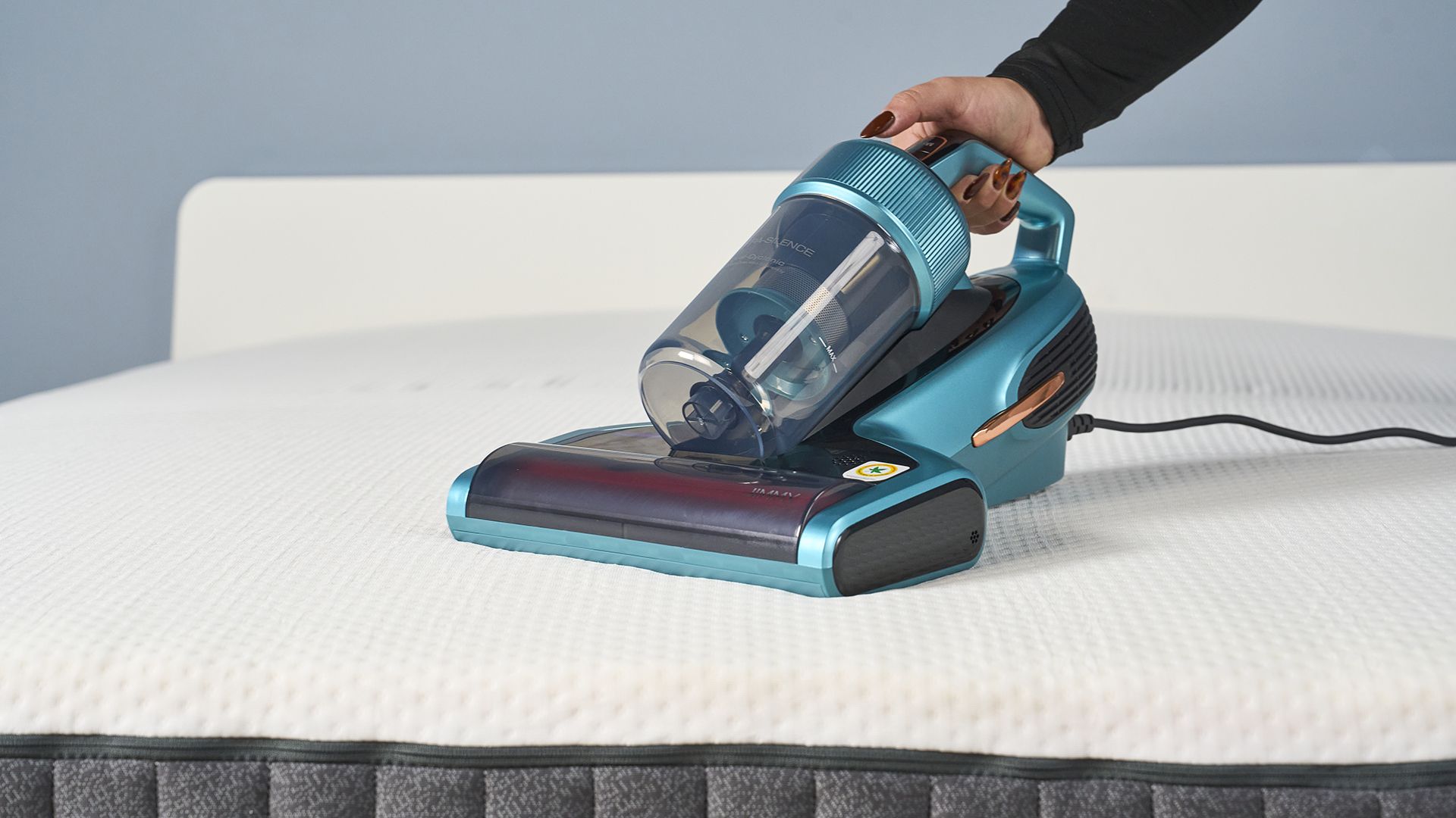 A close up of a hand holding the Jimmy Mattress Vacuum Cleaner and using it to clean the surface of a mattress